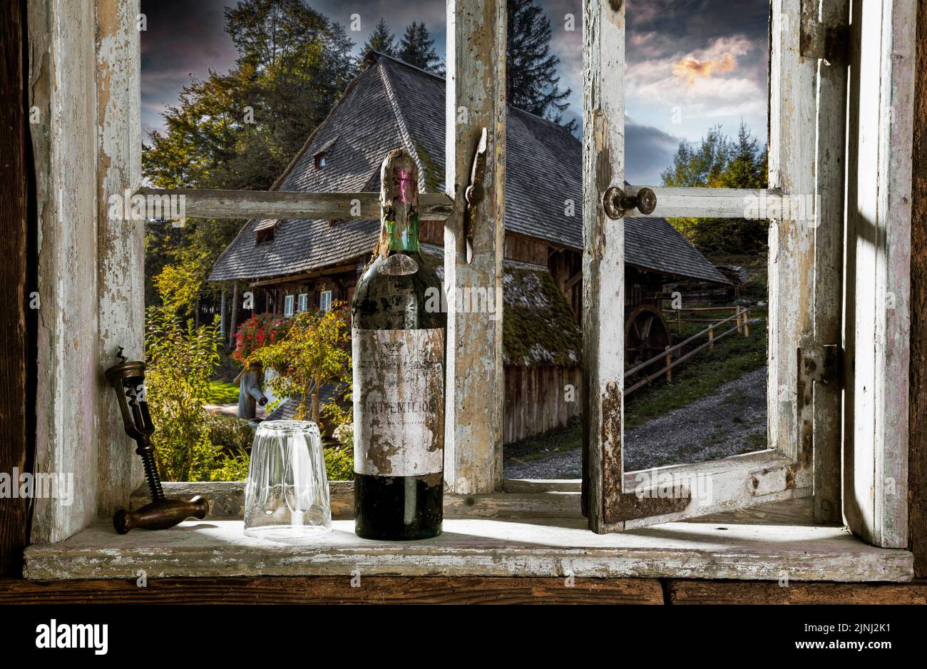 Vista a través de una ventana rústica de madera con una botella de vino antigua en un histórico molino de agua Foto de stock