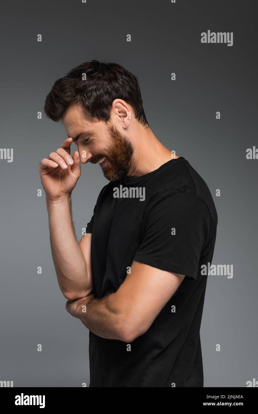 vista lateral del hombre alegre en camiseta negra sonriendo aislada sobre imagen de stock gris Foto de stock