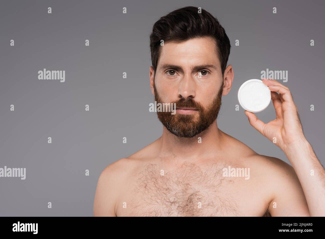 contenedor de mano de hombre barbado y sin camisa con crema cosmética aislado sobre imagen de stock gris Foto de stock