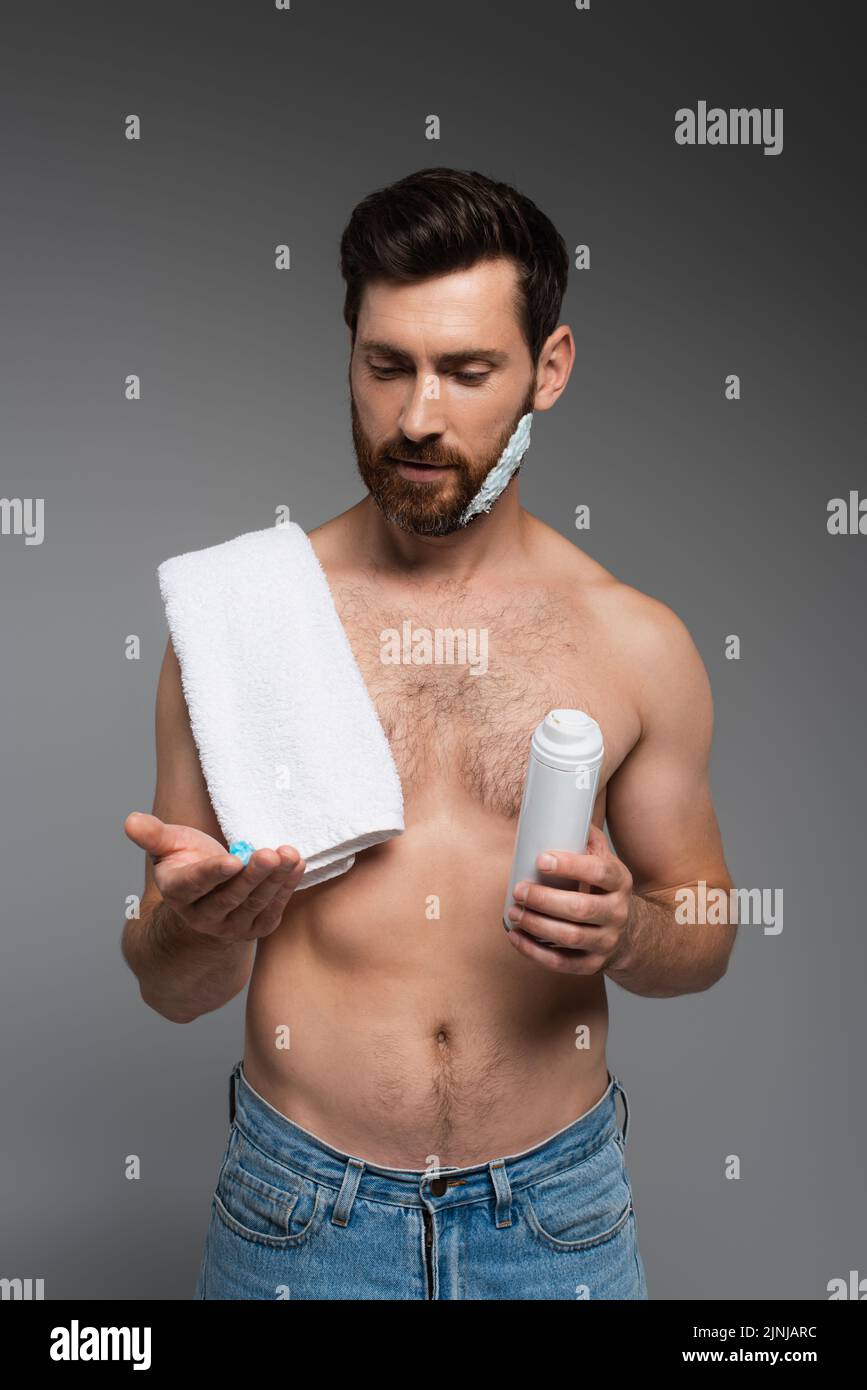 un hombre barbudo con una toalla mirando la espuma de afeitar y la sujeción puede aislarse sobre una imagen de stock gris Foto de stock