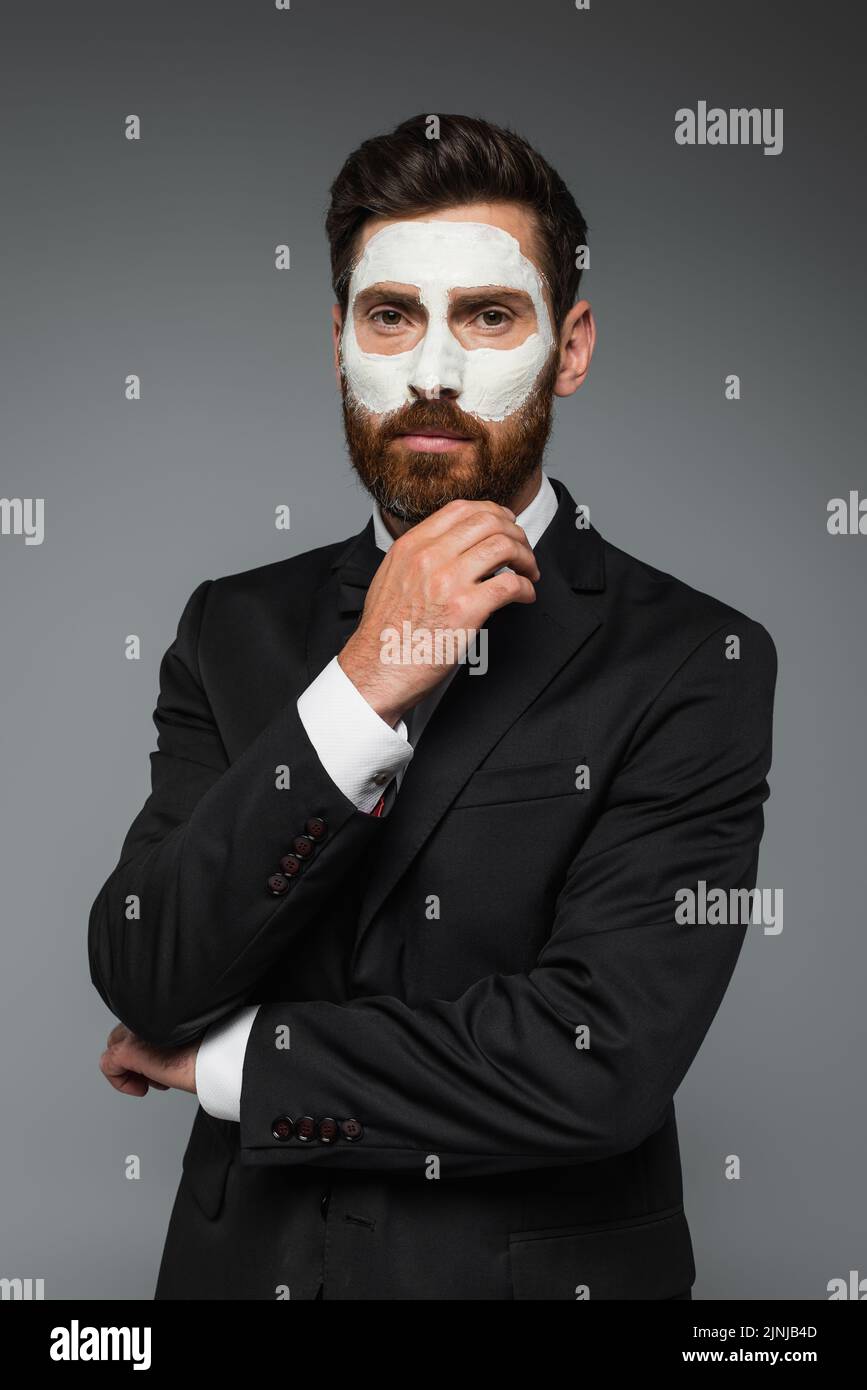 retrato de hombre barbudo en traje con máscara de arcilla en la cara aislado en gris, imagen de archivo Foto de stock