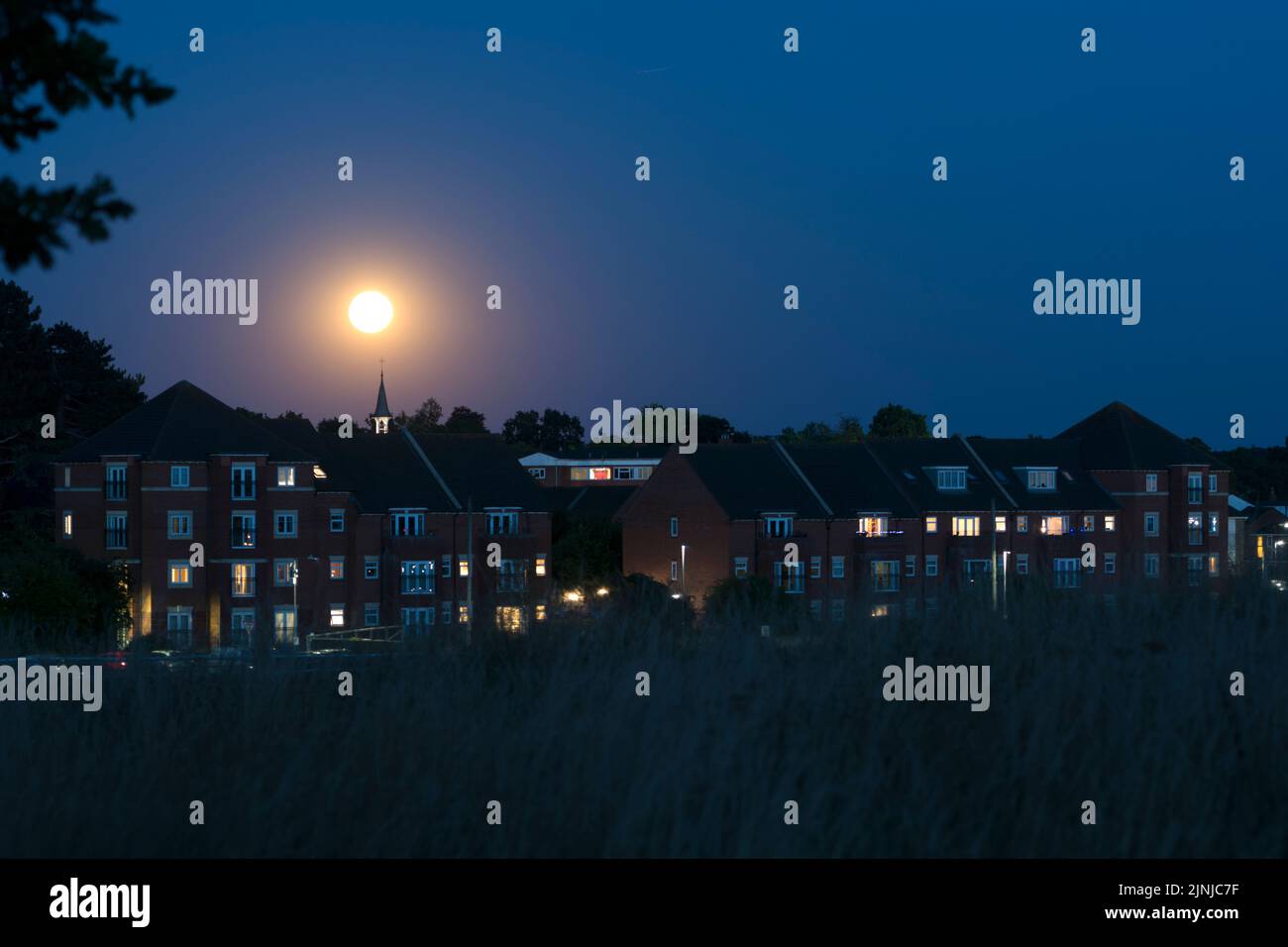 La luna llena se eleva sobre los edificios de apartamentos en Warwick, Warwickshire, Reino Unido Foto de stock