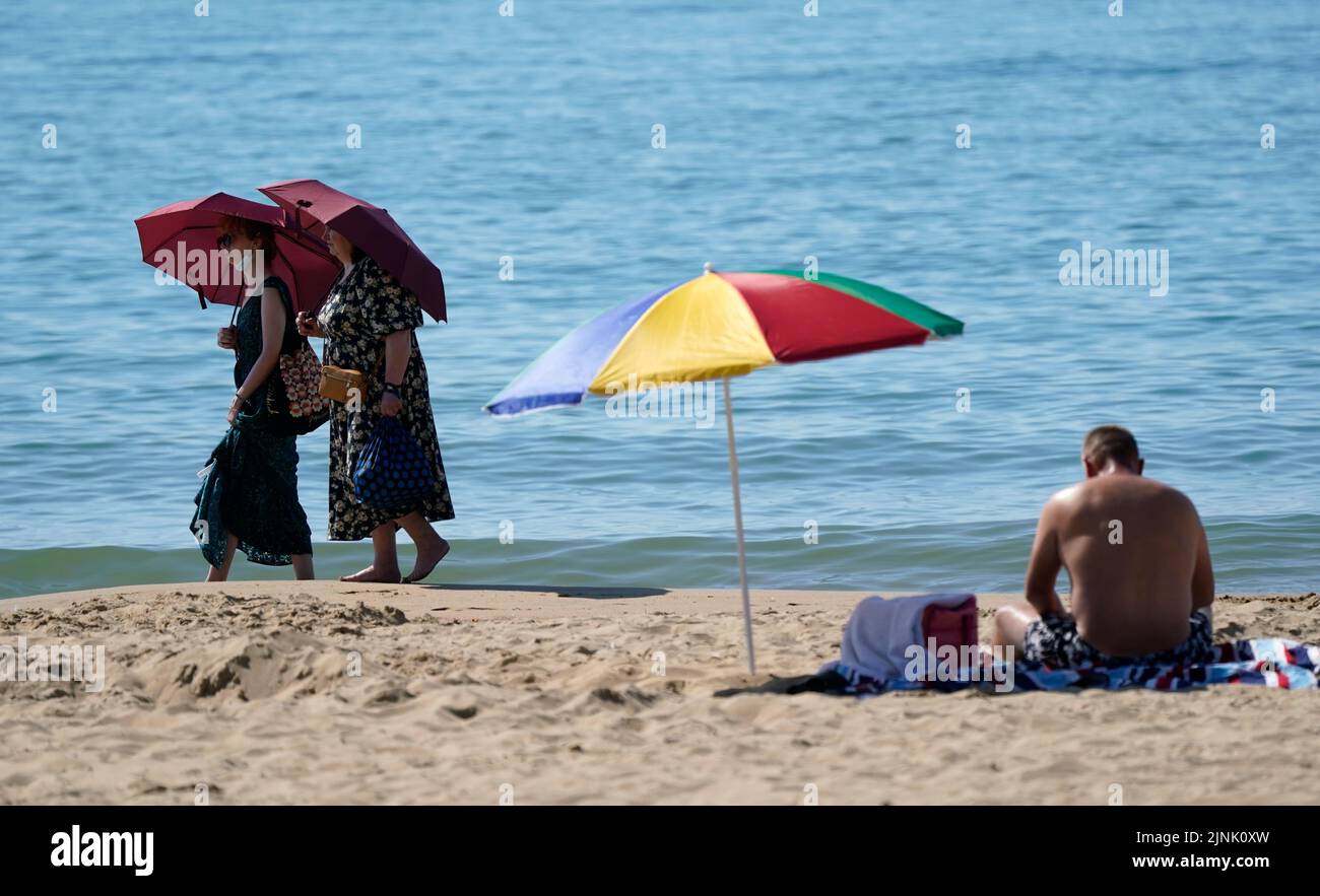 Las personas se refugian bajo sombrillas mientras caminan a lo largo de la playa de Bournemouth en Dorset. Está previsto que se declare una sequía en algunas partes de Inglaterra el viernes, con temperaturas que alcanzarán los 35C grados, lo que hace que el país sea más caliente que algunas partes del Caribe. Fecha de la foto: Viernes 12 de agosto de 2022. Foto de stock