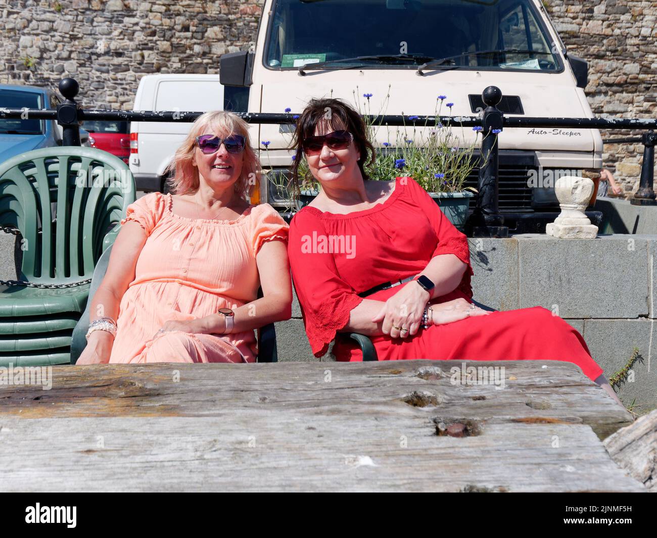 Conwy, Clwyd, Gales, agosto de 07 2022: Dos elegantes damas se sientan juntas y sonríen para una foto en el puerto. Foto de stock