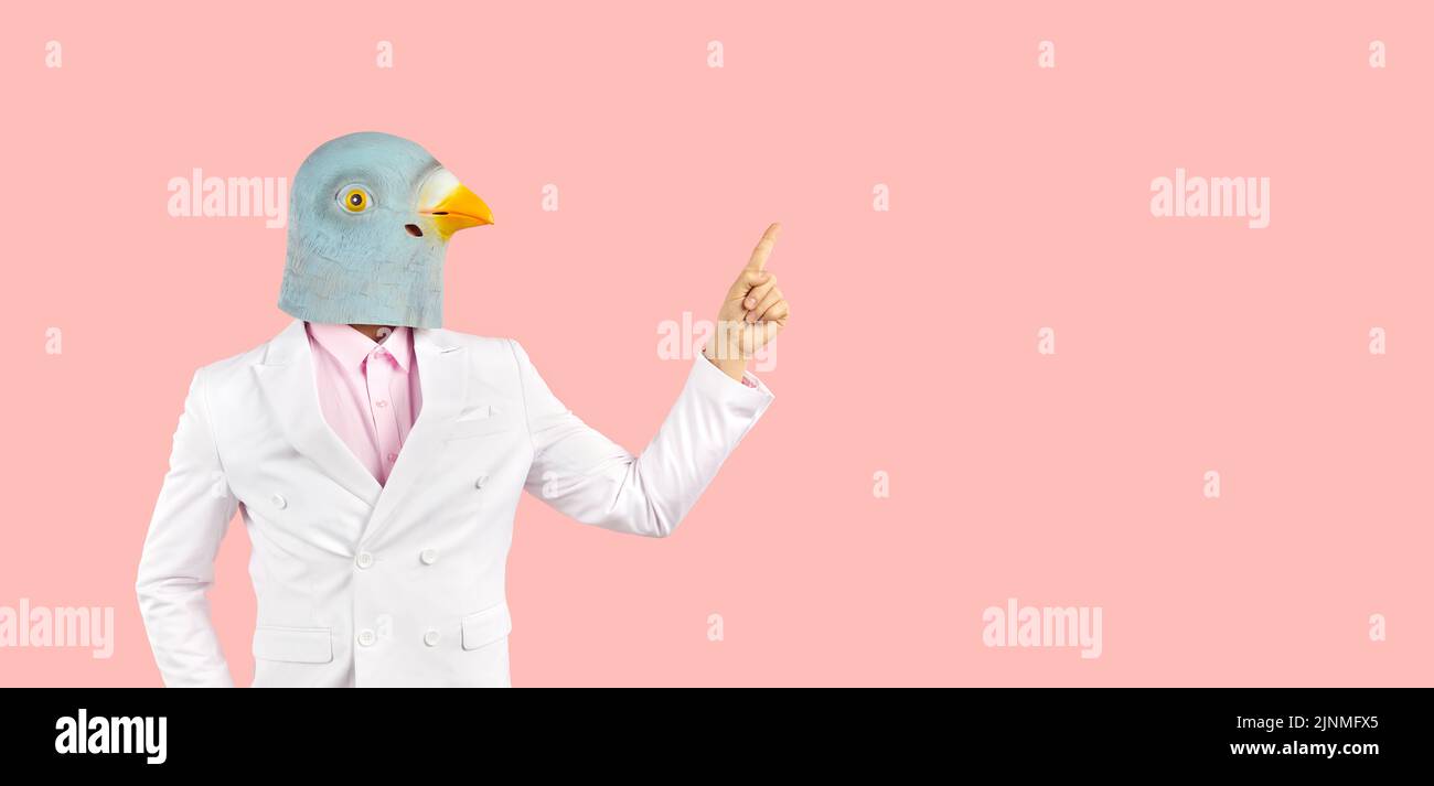 Extraño tipo en gracioso paloma máscara señalando su dedo en el espacio de copia en color rosa banner de fondo Foto de stock