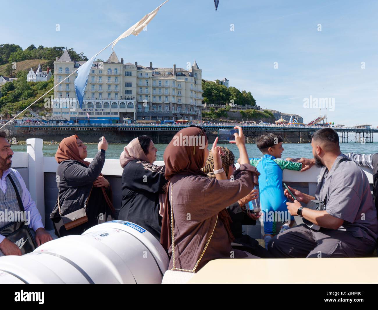 Llandudno, Clwyd, Gales, agosto de 07 2022: Gente disfrutando de un viaje en barco y tomando fotos con el Grand Hotel y el muelle al fondo. Foto de stock