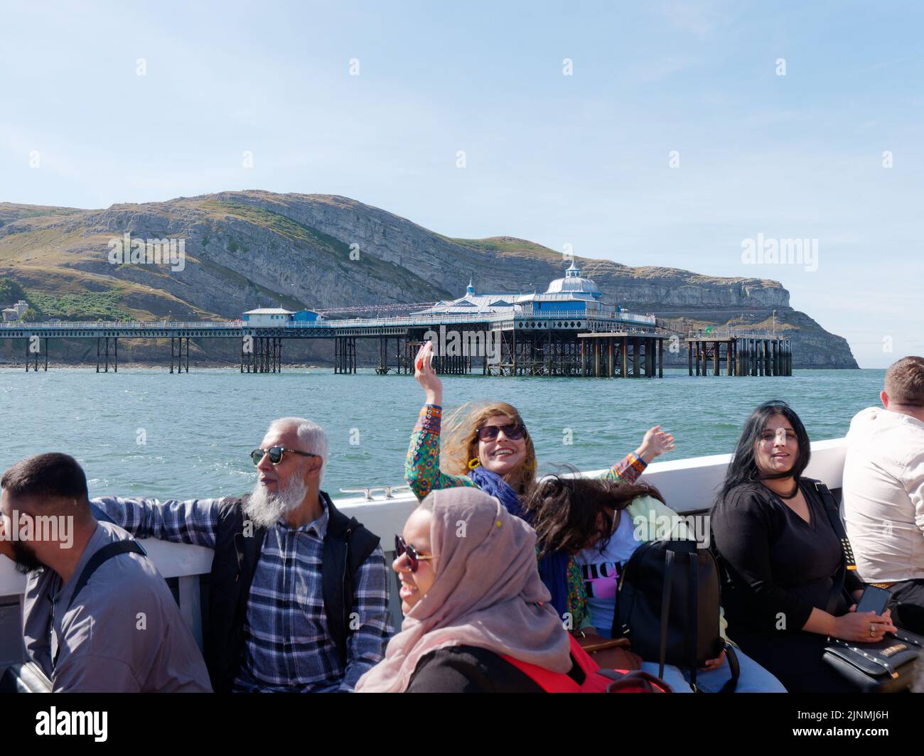 Llandudno, Clwyd, Gales, agosto de 07 2022: La gente disfrutando de un viaje en barco, una señora levanta las manos y sonríe con el muelle y la Gran Orme en el fondo Foto de stock