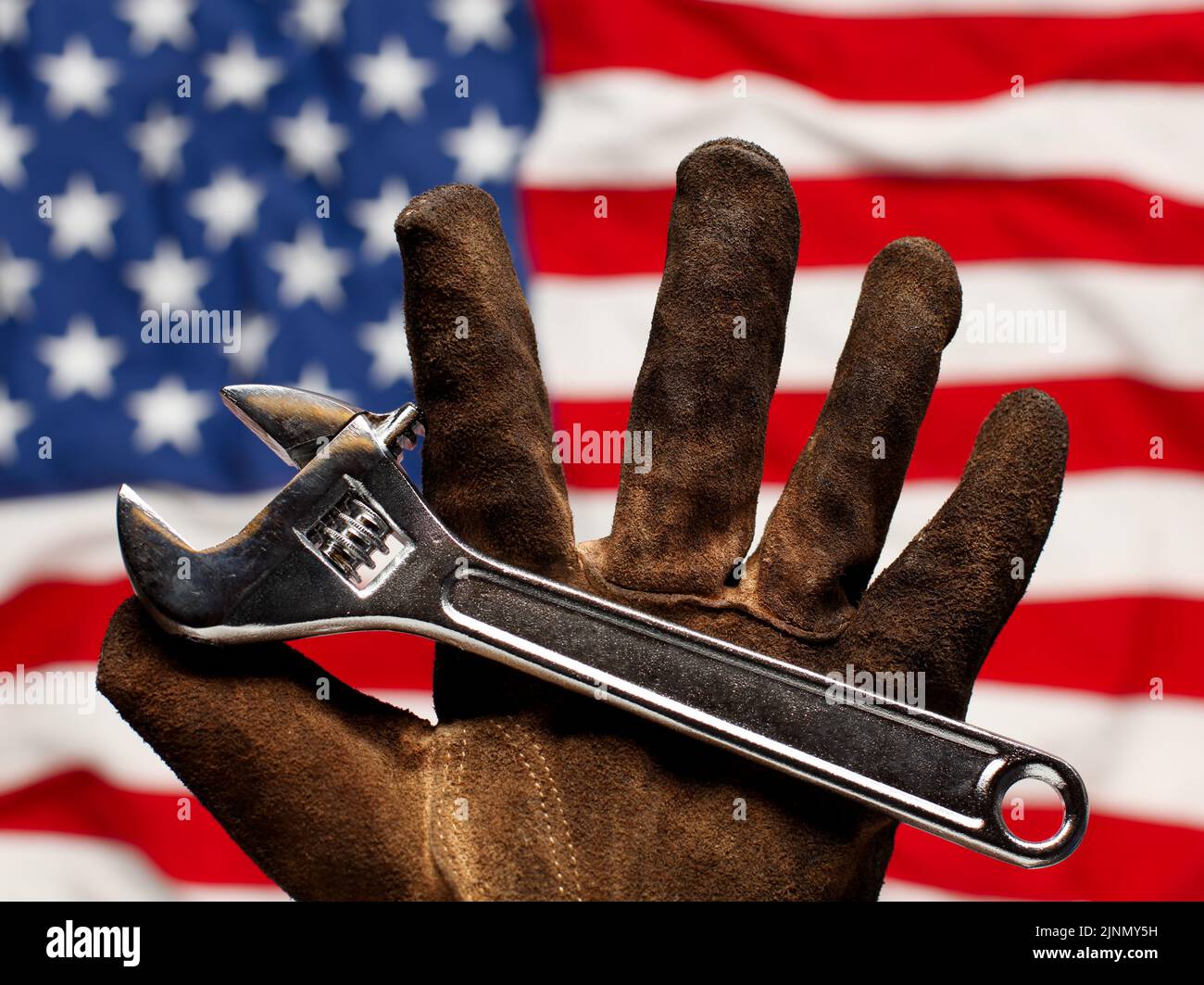 Guante de trabajo viejo y desgastado sujetando la llave ajustable sobre la bandera estadounidense. Concepto de trabajo, trabajo y empleo estadounidense. Foto de stock