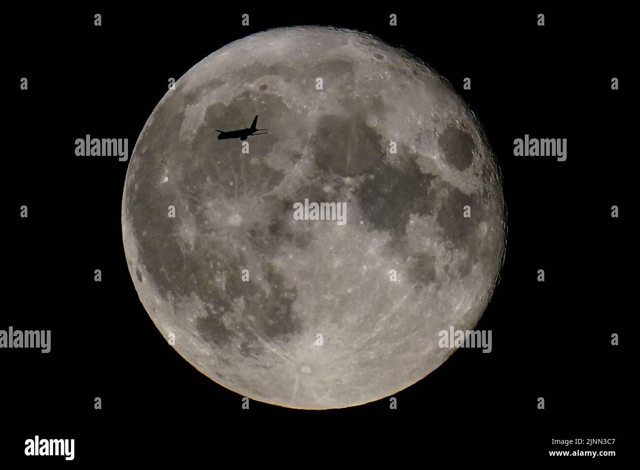 Un avión pasa delante de la superluna Sturgeon, la superluna final del año, sobre el este de Londres. Fecha de la foto: Viernes 12 de agosto de 2022. Foto de stock