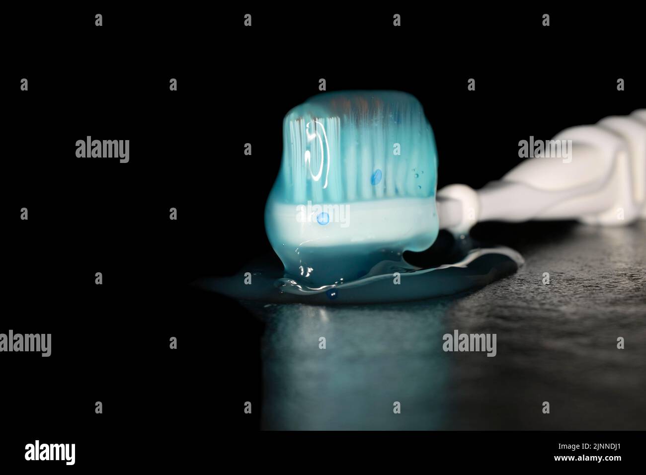 Cepillo de dientes eléctrico con pasta de dientes azul transparente, fotografía de estudio con fondo negro Foto de stock