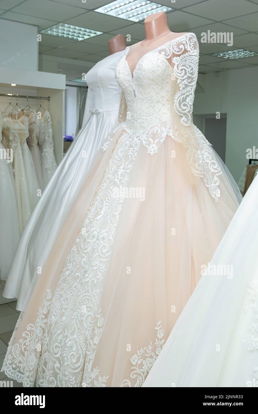 Un hermoso de boda de color crema sobre un maniquí. Un vestido de la boda en el fondo de otros vestidos de la boda en un salón de la boda Fotografía