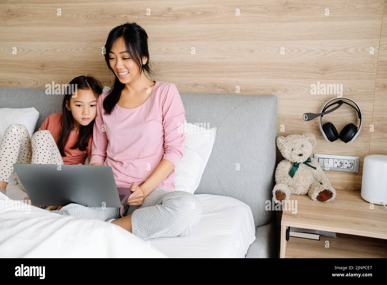 Madre asiática y su hija usando el ordenador portátil mientras se sientan en la cama en casa Foto de stock