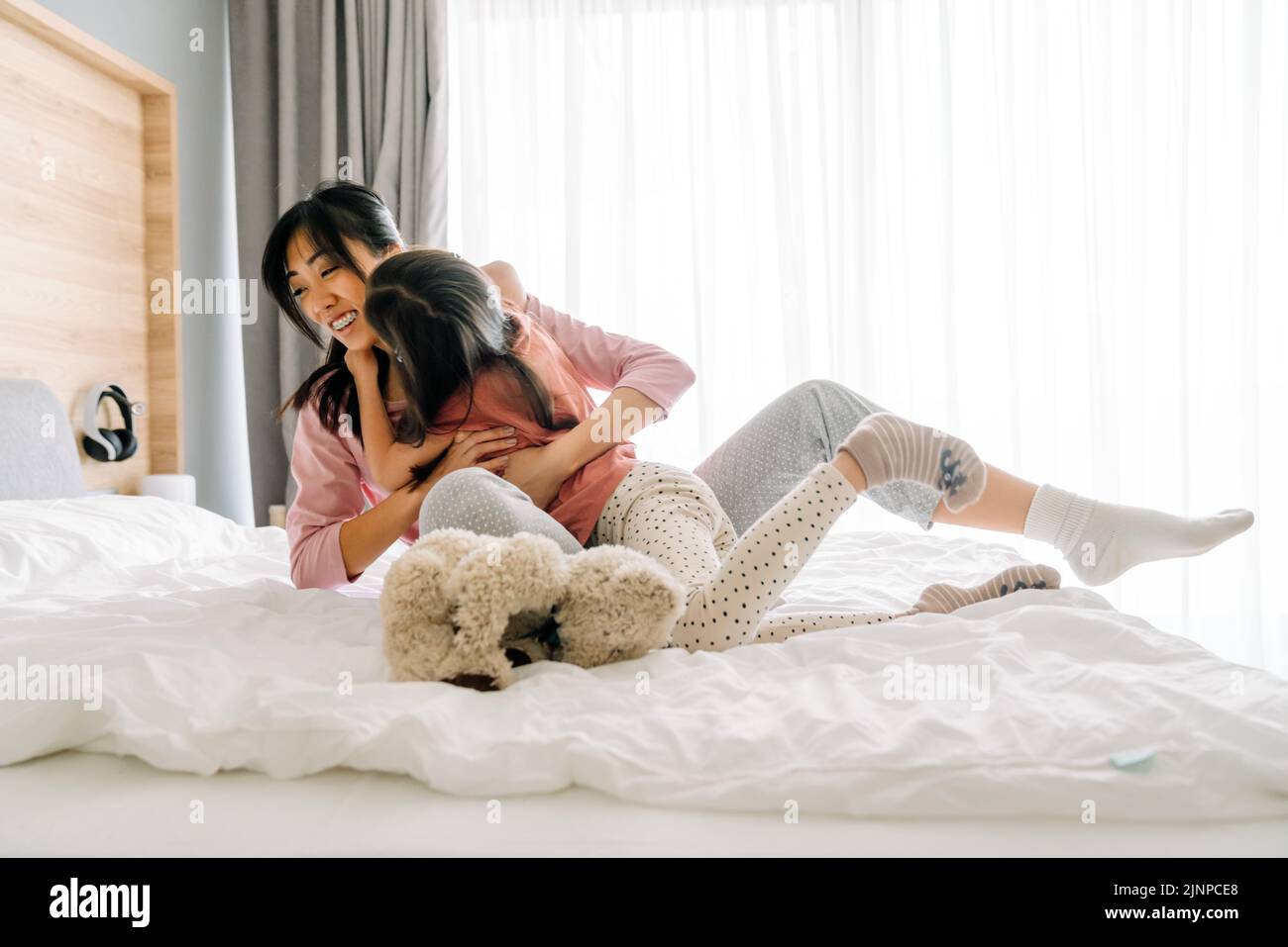 Madre e hija asiáticas riendo mientras se divierten en la cama en casa Foto de stock