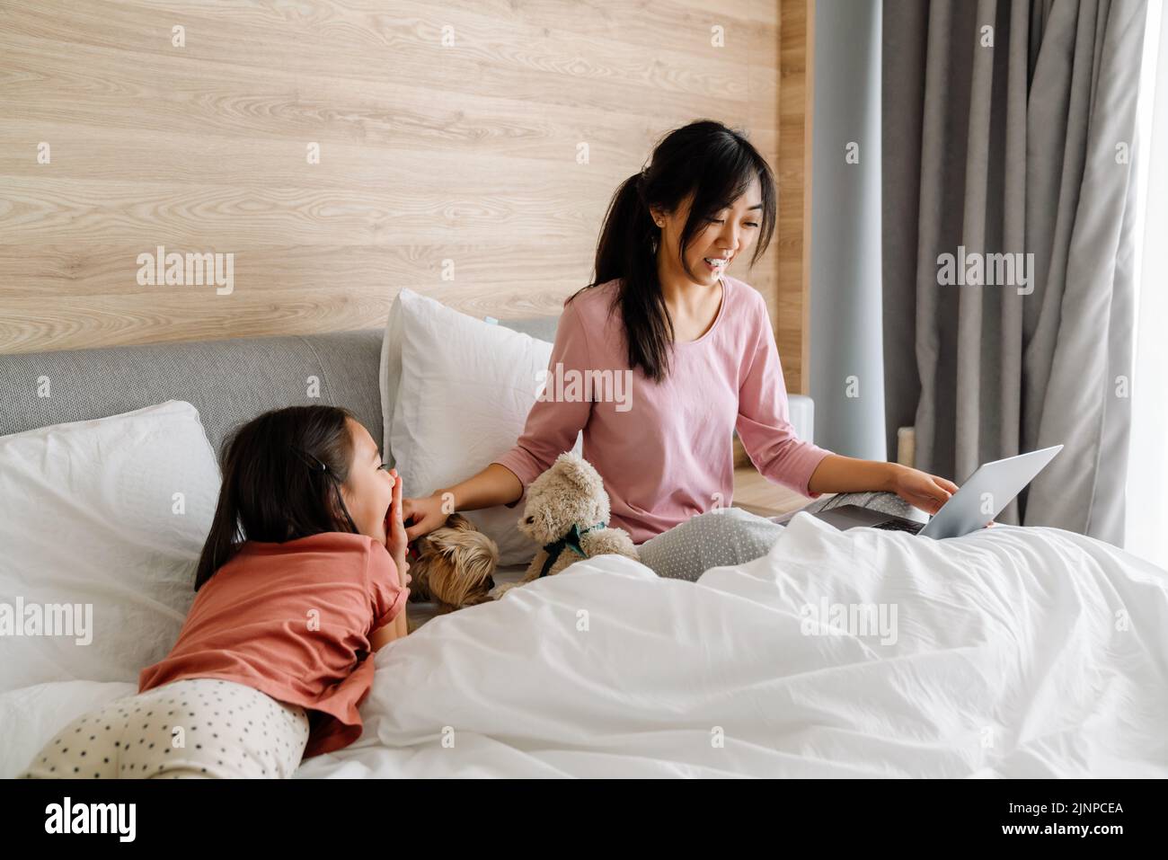 Madre asiática y su hija usando el ordenador portátil mientras se sientan en la cama en casa Foto de stock