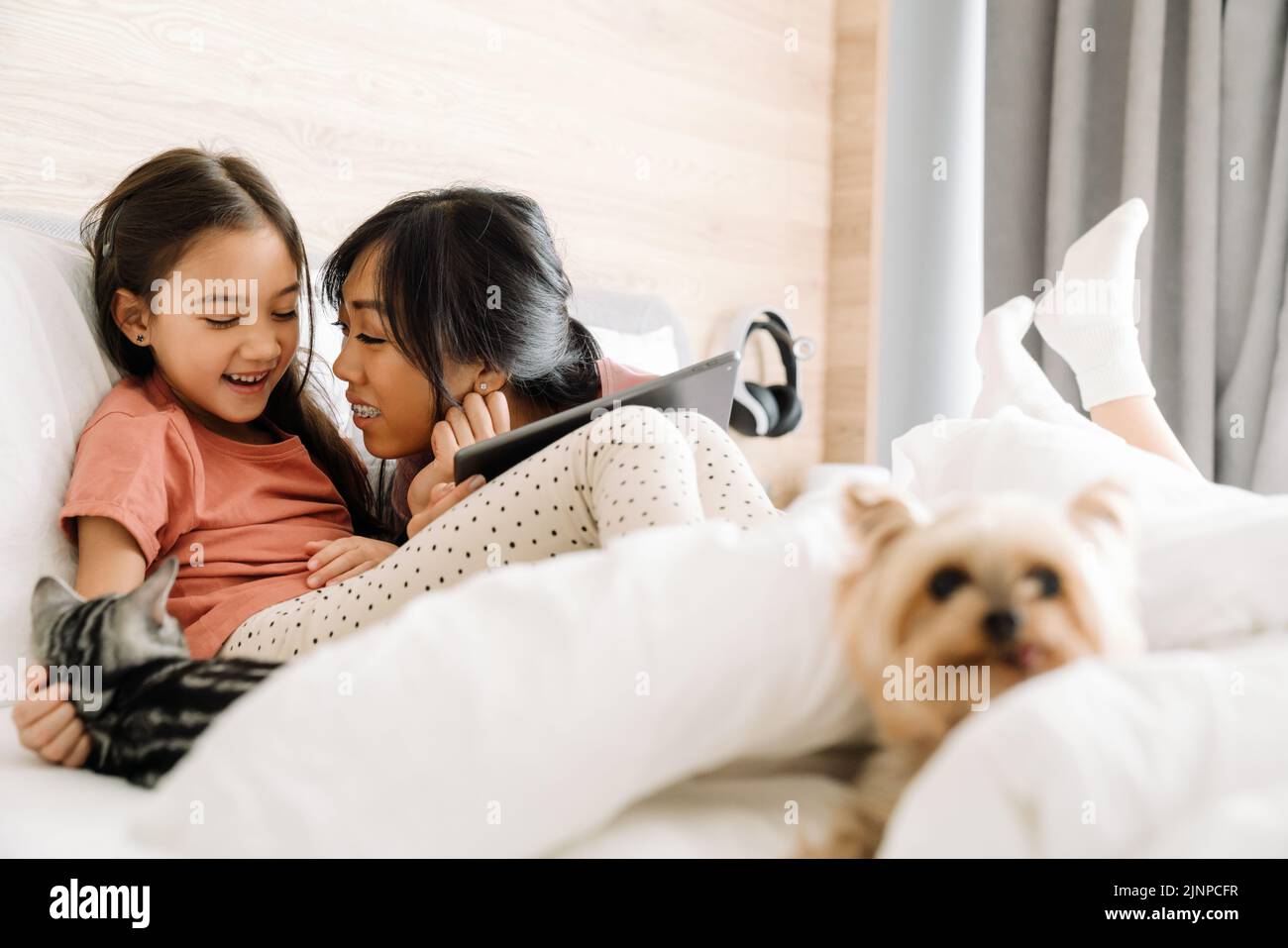 Madre asiática y su hija usando una tableta mientras se sienta en la cama en casa Foto de stock