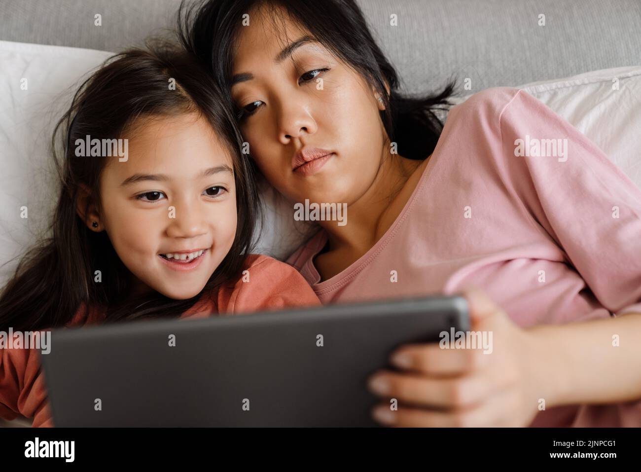 Mujer asiática y su hija usando una tableta mientras se acuesta en la cama en casa Foto de stock