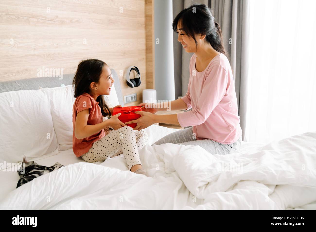 Mujer asiática dando a su hija regalo mientras se sienta en la cama en casa Foto de stock