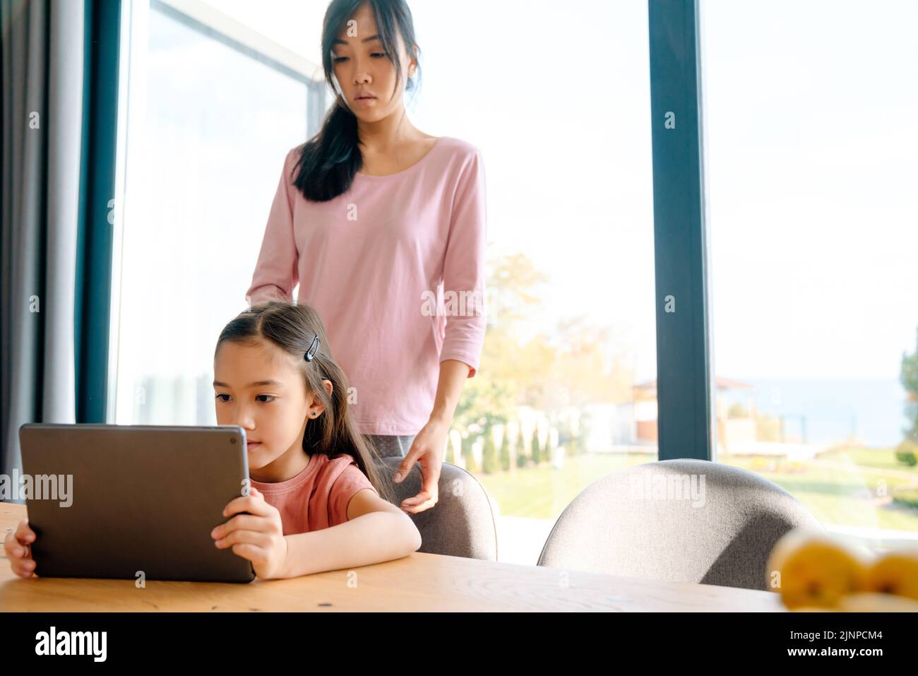 Mujer asiática y su hija usando una tableta mientras pasan tiempo juntos en casa Foto de stock