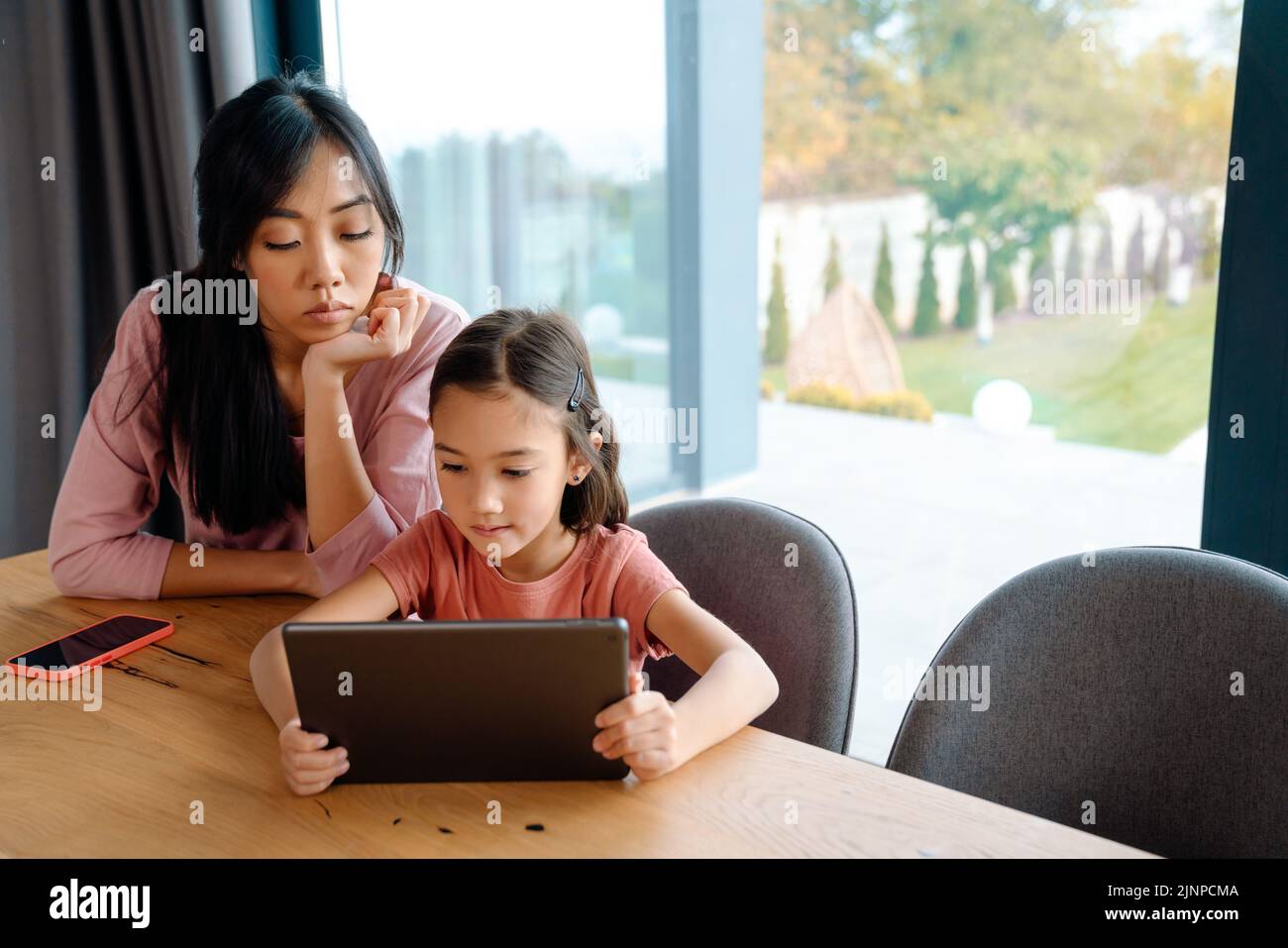 Mujer asiática y su hija usando una tableta mientras estaba sentada en la mesa de casa Foto de stock