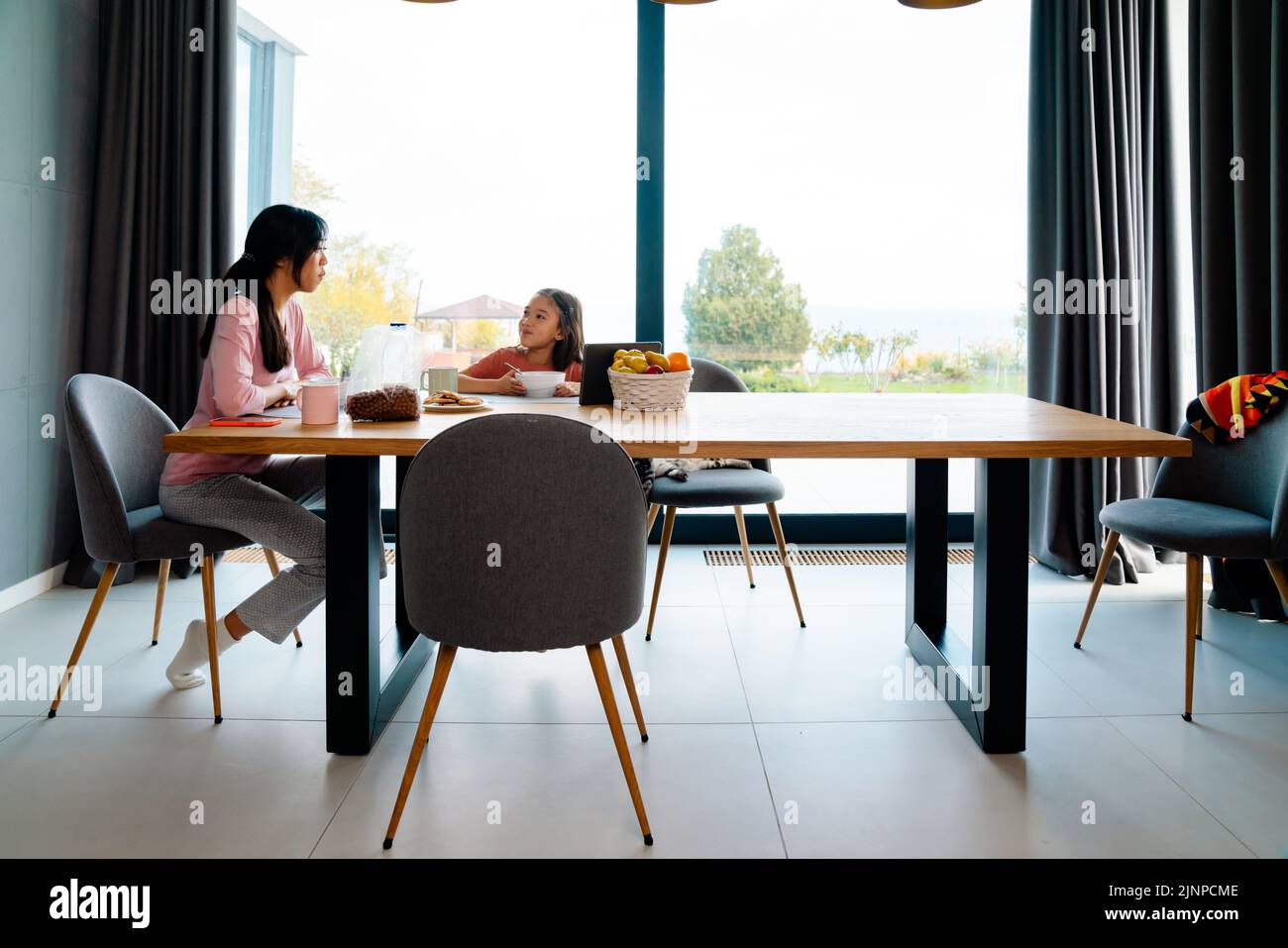 Chica asiática utilizando la tableta mientras desayuna con su madre en casa Foto de stock