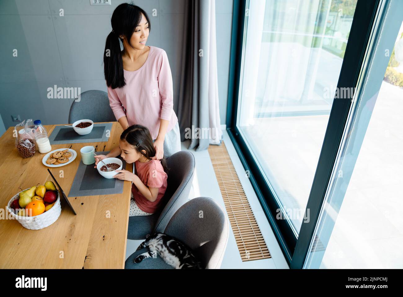 Chica asiática utilizando la tableta mientras desayuna con su madre en casa Foto de stock