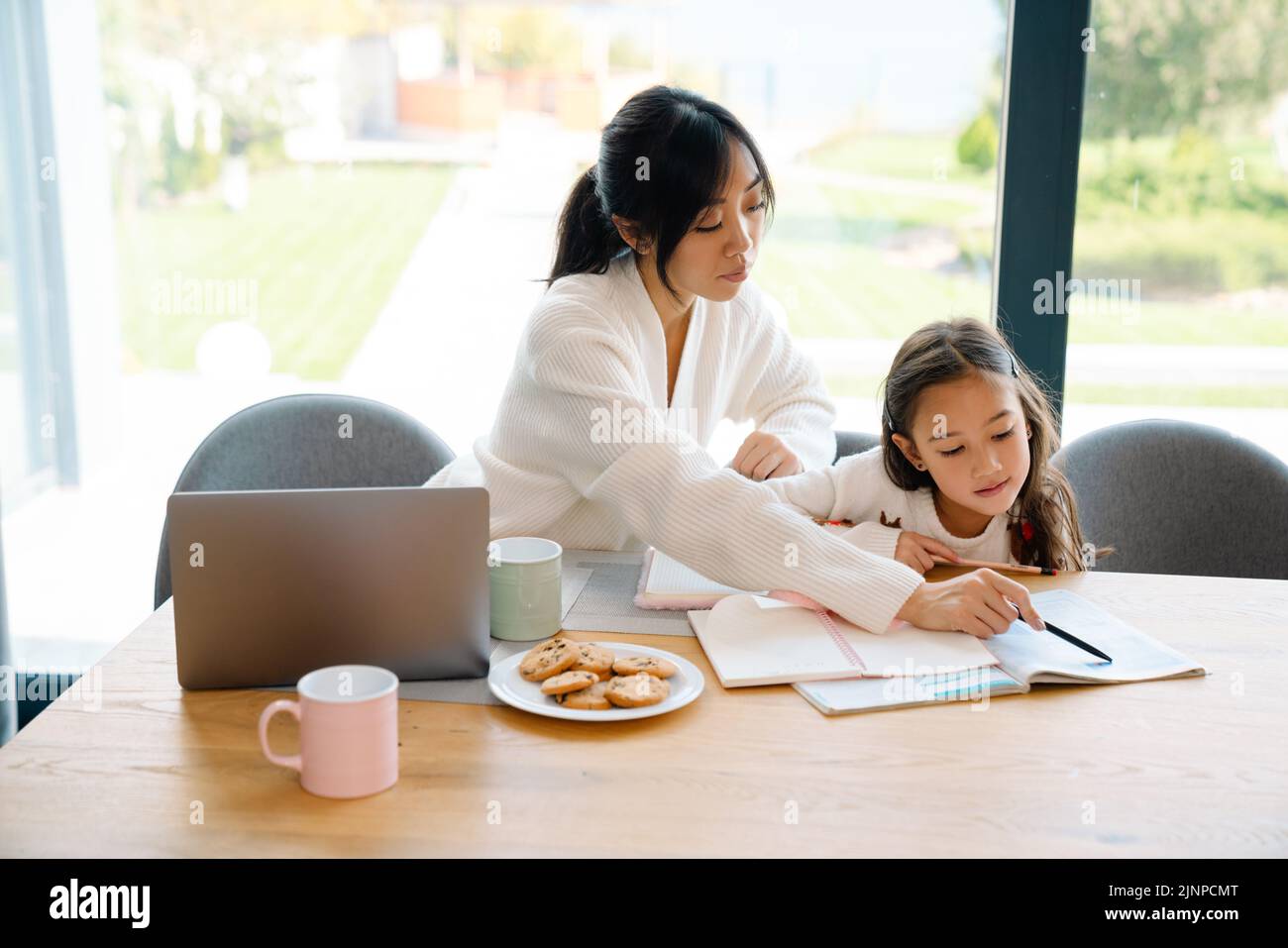 Chica asiática haciendo la tarea con su madre en la cocina en casa Foto de stock