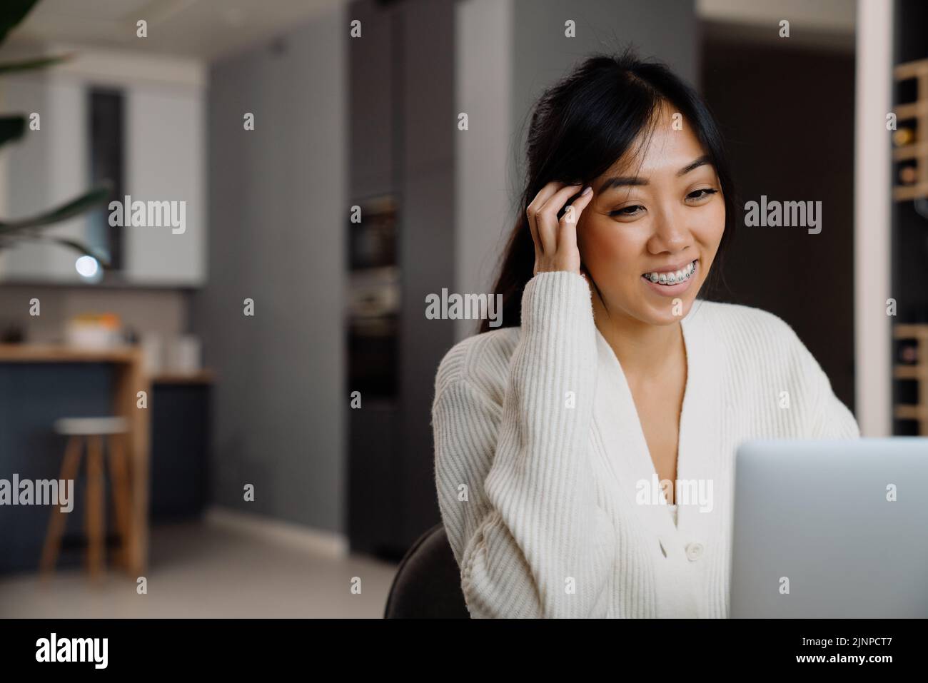 Mujer asiática con corsé riendo mientras trabaja con el portátil en casa Foto de stock