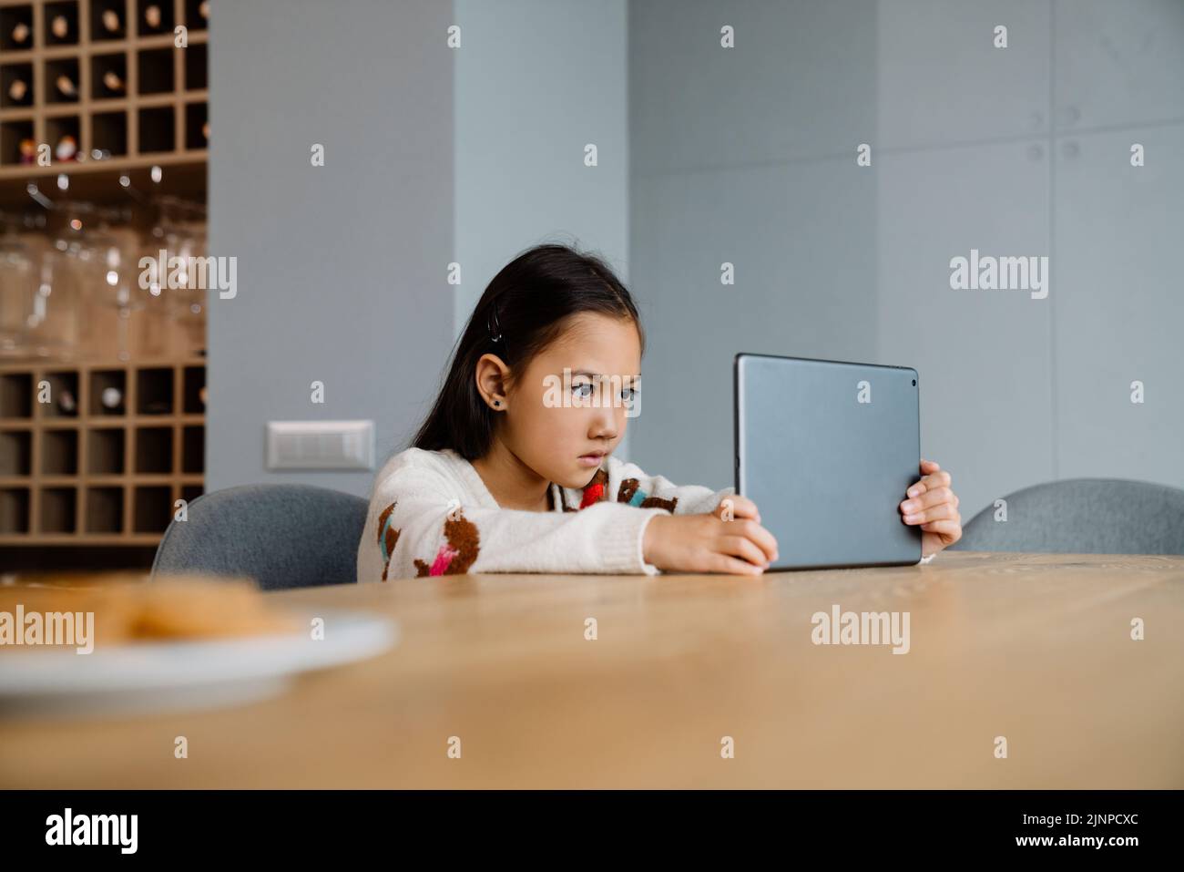 Chica asiática utilizando la tableta de ordenador mientras se sienta en la mesa en casa Foto de stock