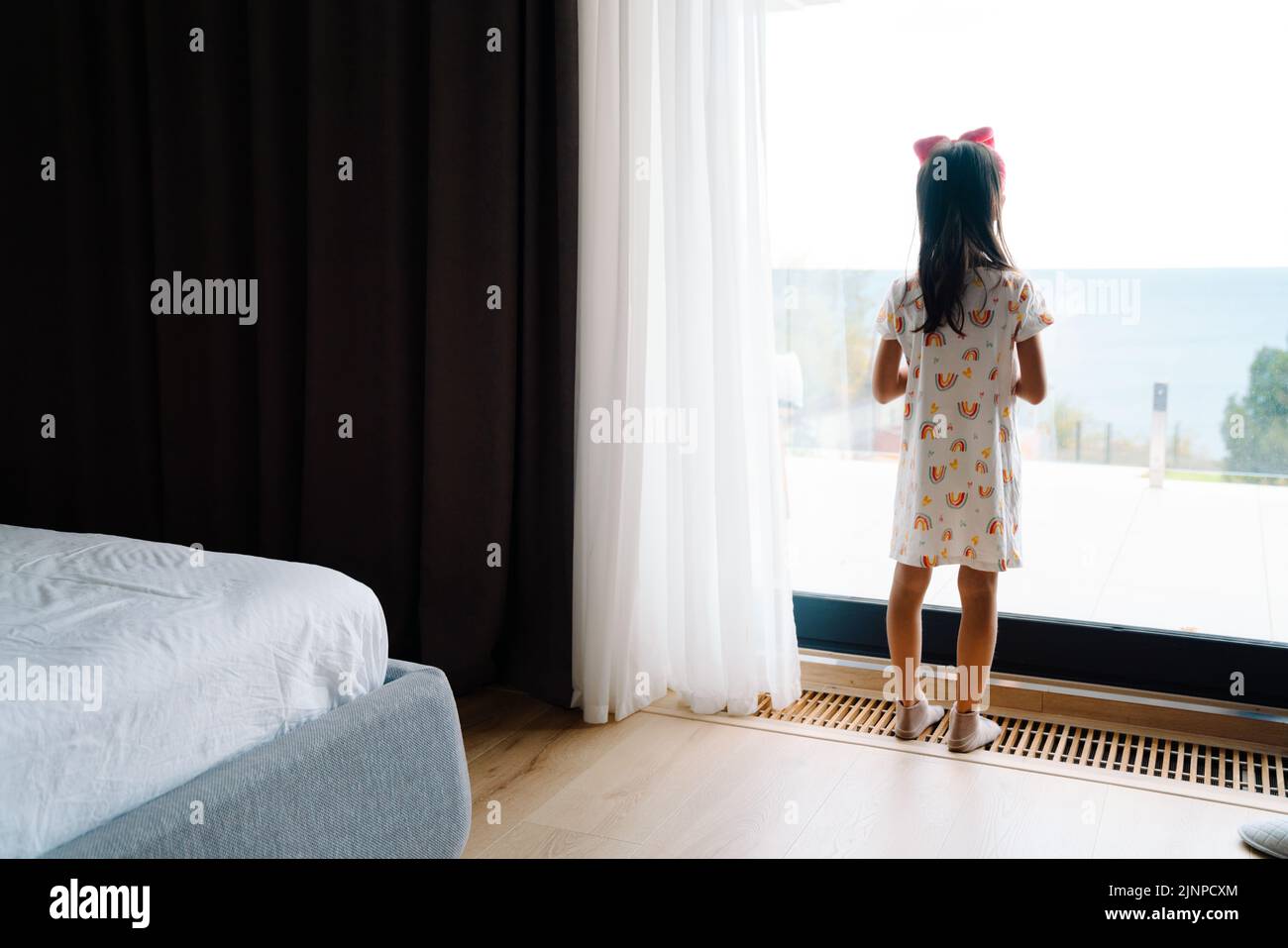 Chica asiática que usa ropa para el hogar mirando por la ventana en el dormitorio de la casa Foto de stock