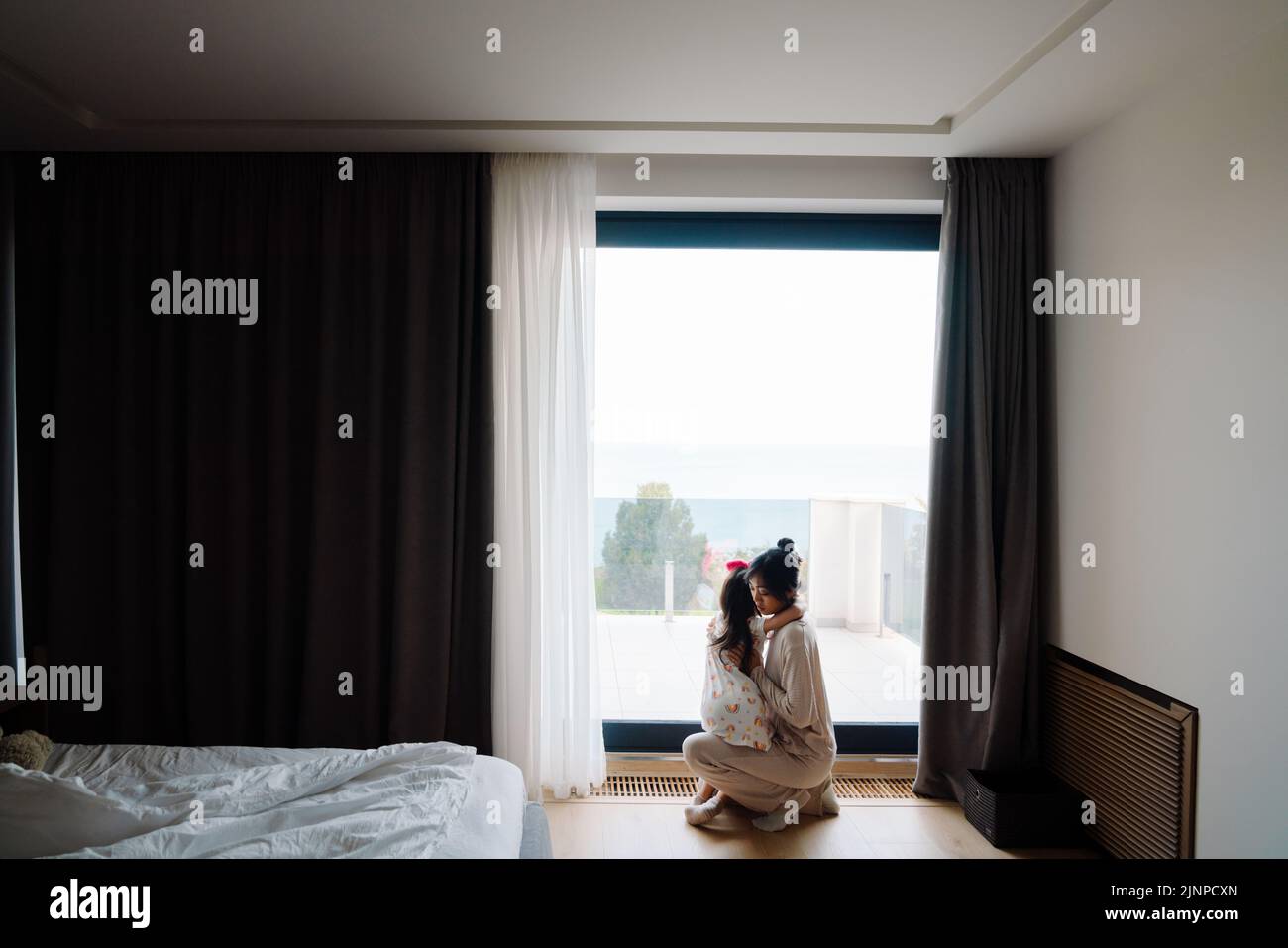 Mujer asiática y su hija mirando por la ventana juntos en casa Foto de stock
