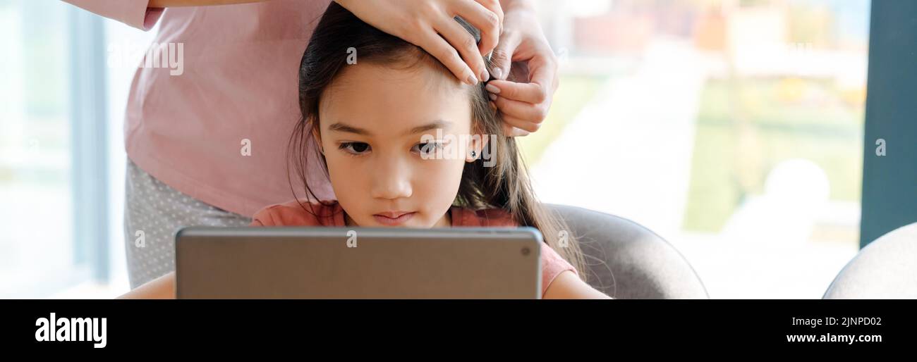 Mujer asiática y su hija usando una tableta mientras pasan tiempo juntos en casa Foto de stock