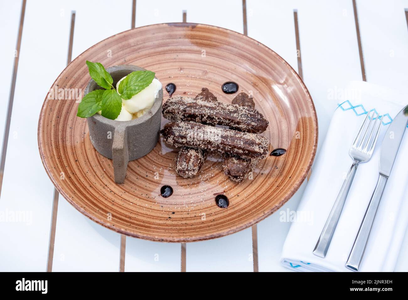 Churros de chocolate con helado sobre un plato de porcelana marrón Foto de stock