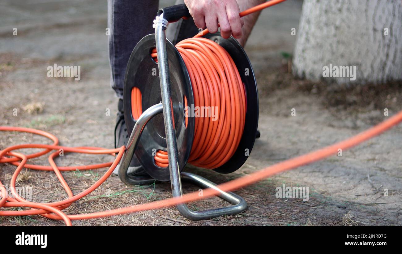 Un hombre enrolla el cable con un carrete de cable eléctrico Foto de stock
