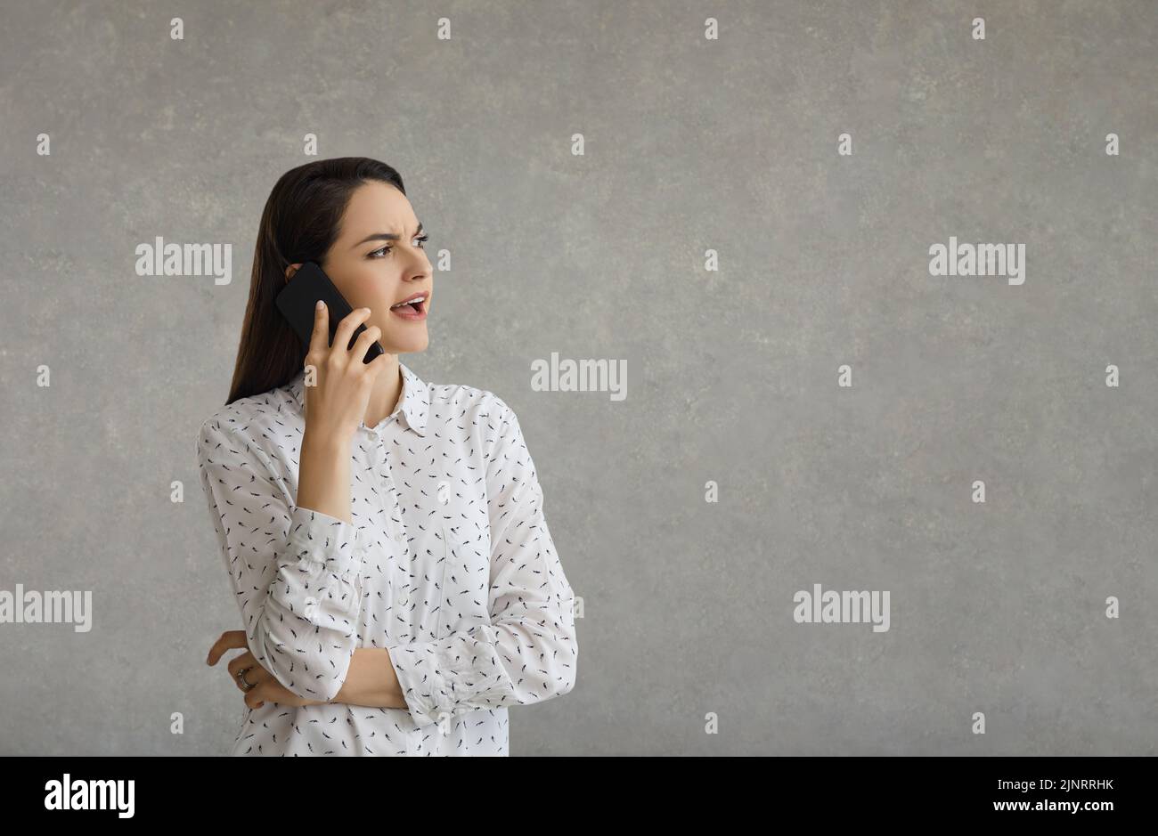 Retrato de una mujer casual sonriente hablando por teléfono mientras estaba de pie sobre fondo gris Foto de stock