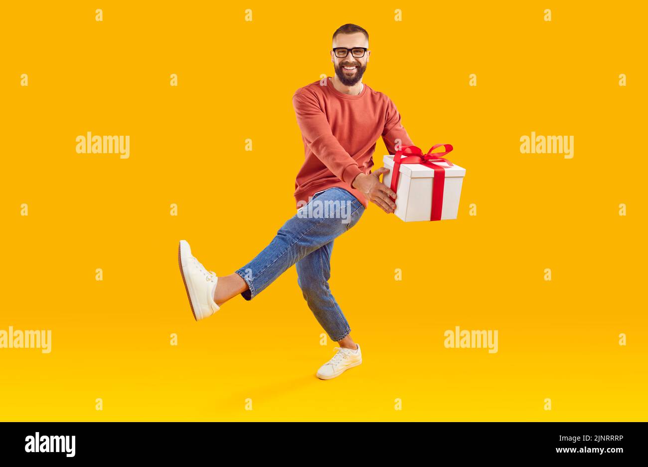 Retrato de un joven feliz y sonriente con caja de regalo bailando sobre fondo amarillo de estudio Foto de stock