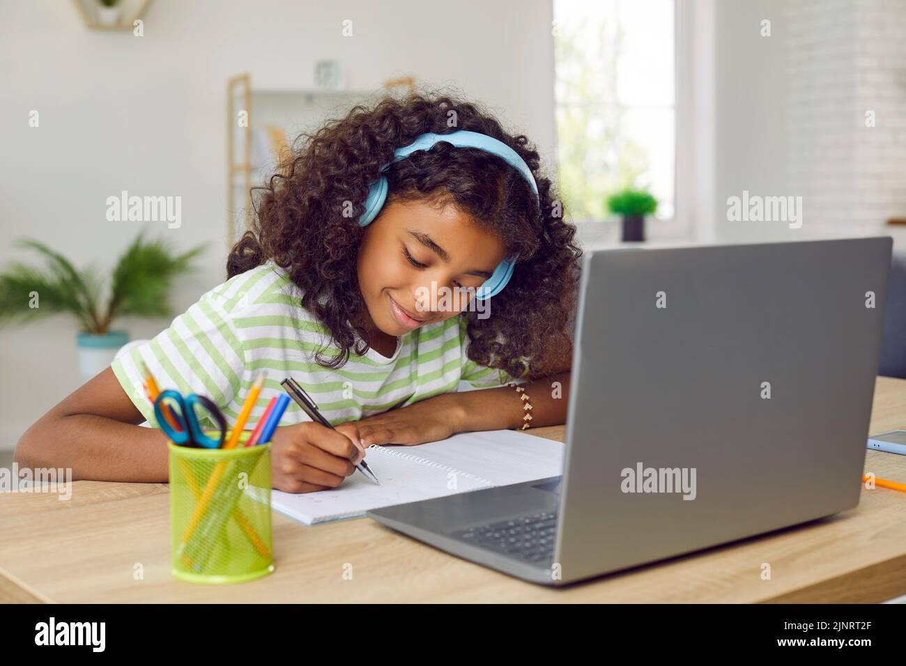 Niño escolar feliz sentado en el escritorio con el ordenador portátil, teniendo clase en línea y escribiendo en el portátil Foto de stock