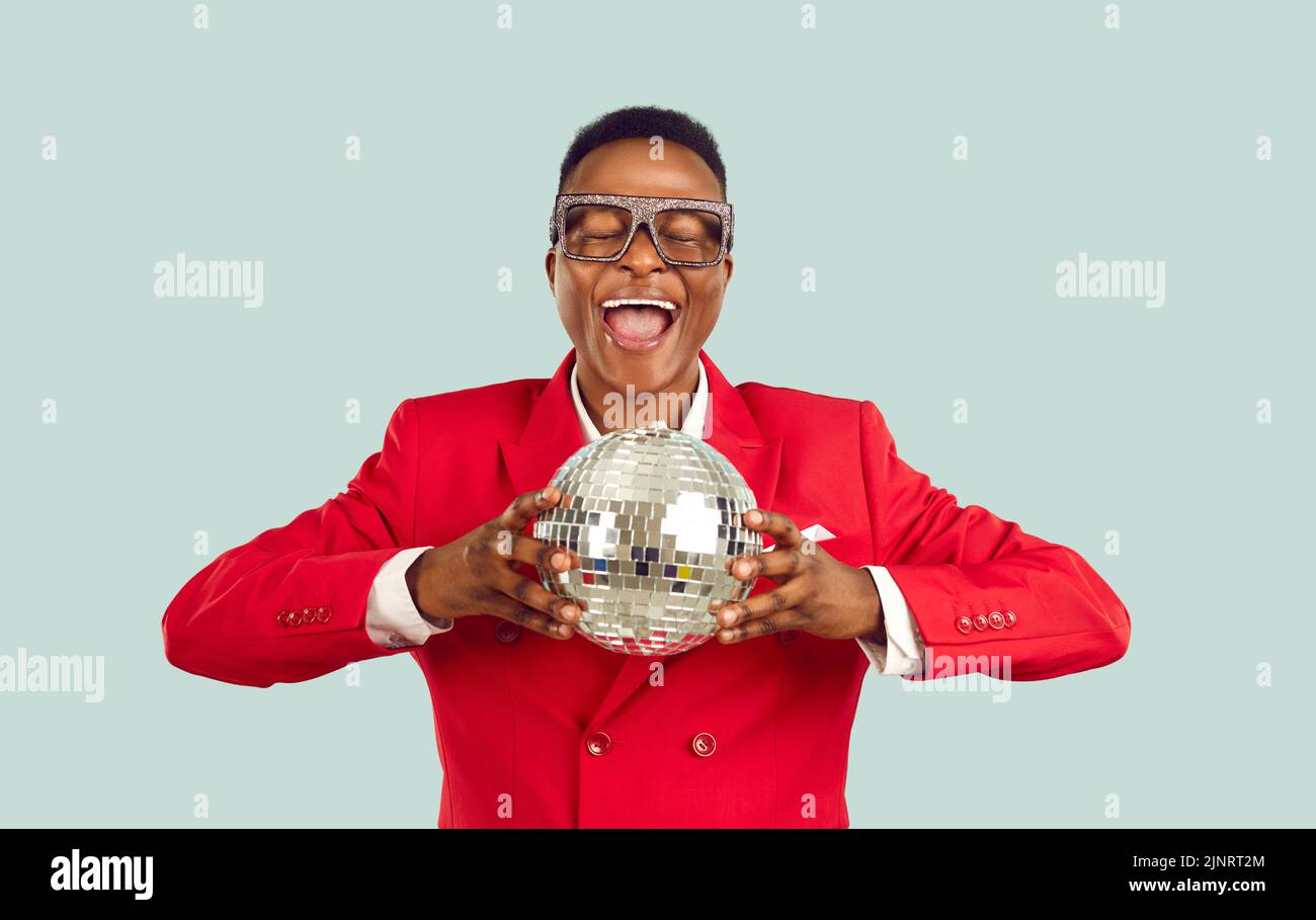 Joven hombre africano-americano animador con gafas con estilo y traje rojo embrague bola disco para la fiesta Foto de stock