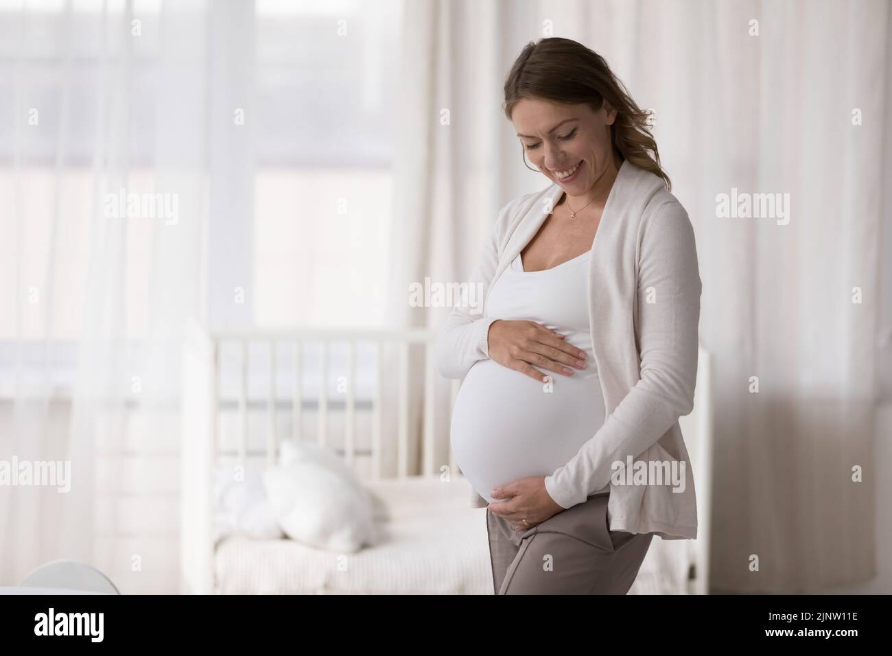 Mujer embarazada joven abrazando acariciando su vientre grande, pose adentro Foto de stock