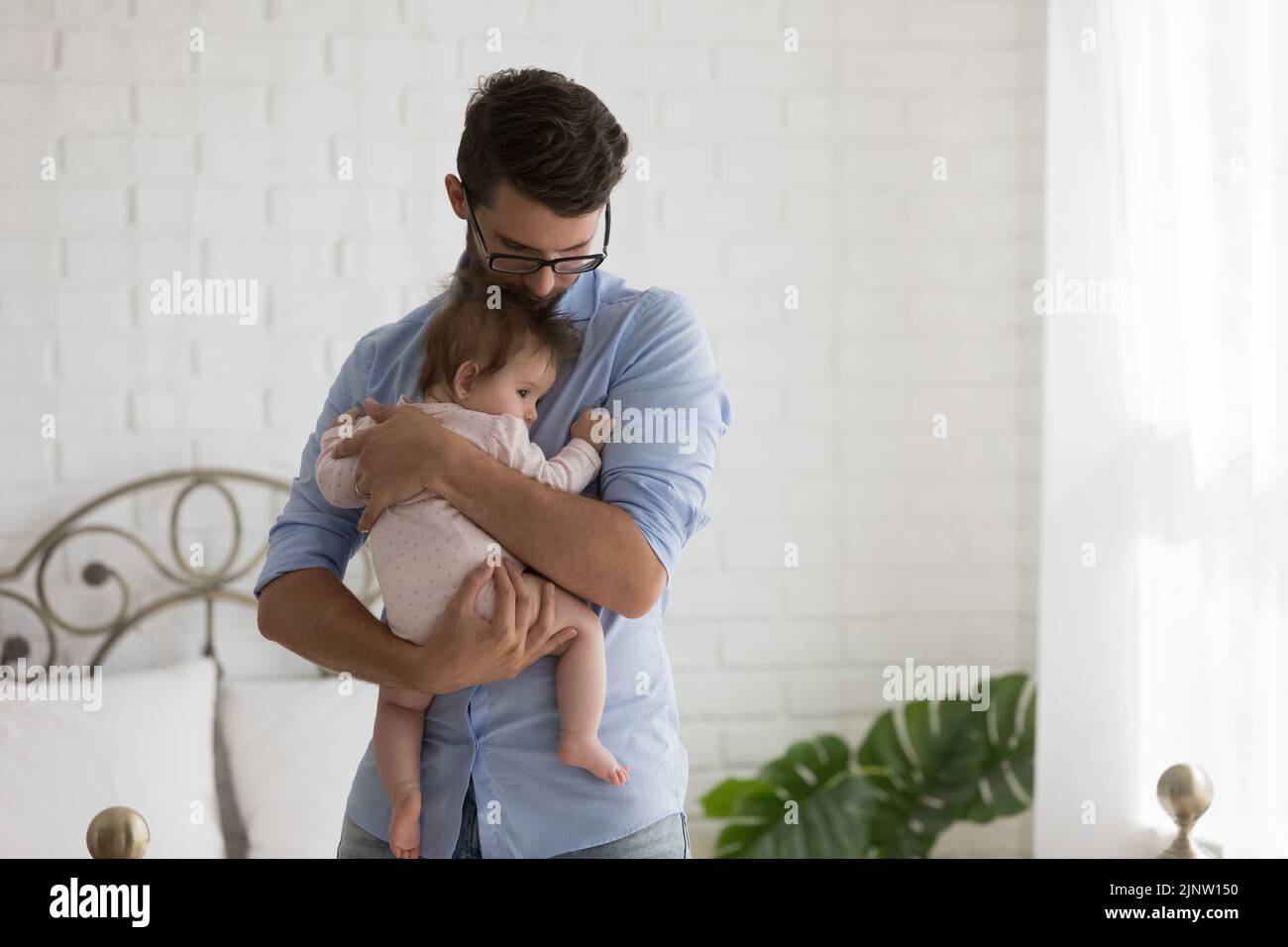 El padre acurruca al bebé recién nacido de pie en un acogedor dormitorio en casa Foto de stock