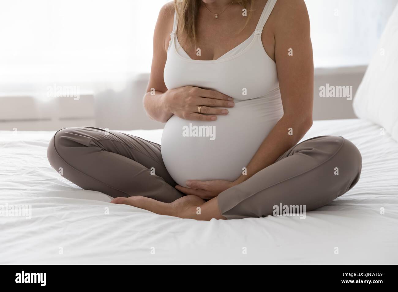 La mujer embarazada se sienta con las piernas cruzadas en la cama toque el vientre Disfrute del embarazo Foto de stock