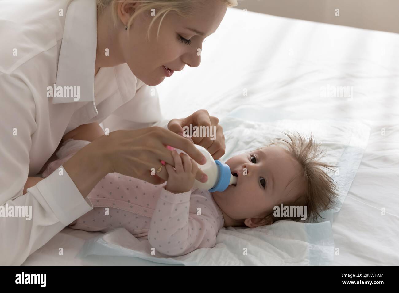 Adorable bebé tumbado en la cama chupando la leche del biberón Foto de stock