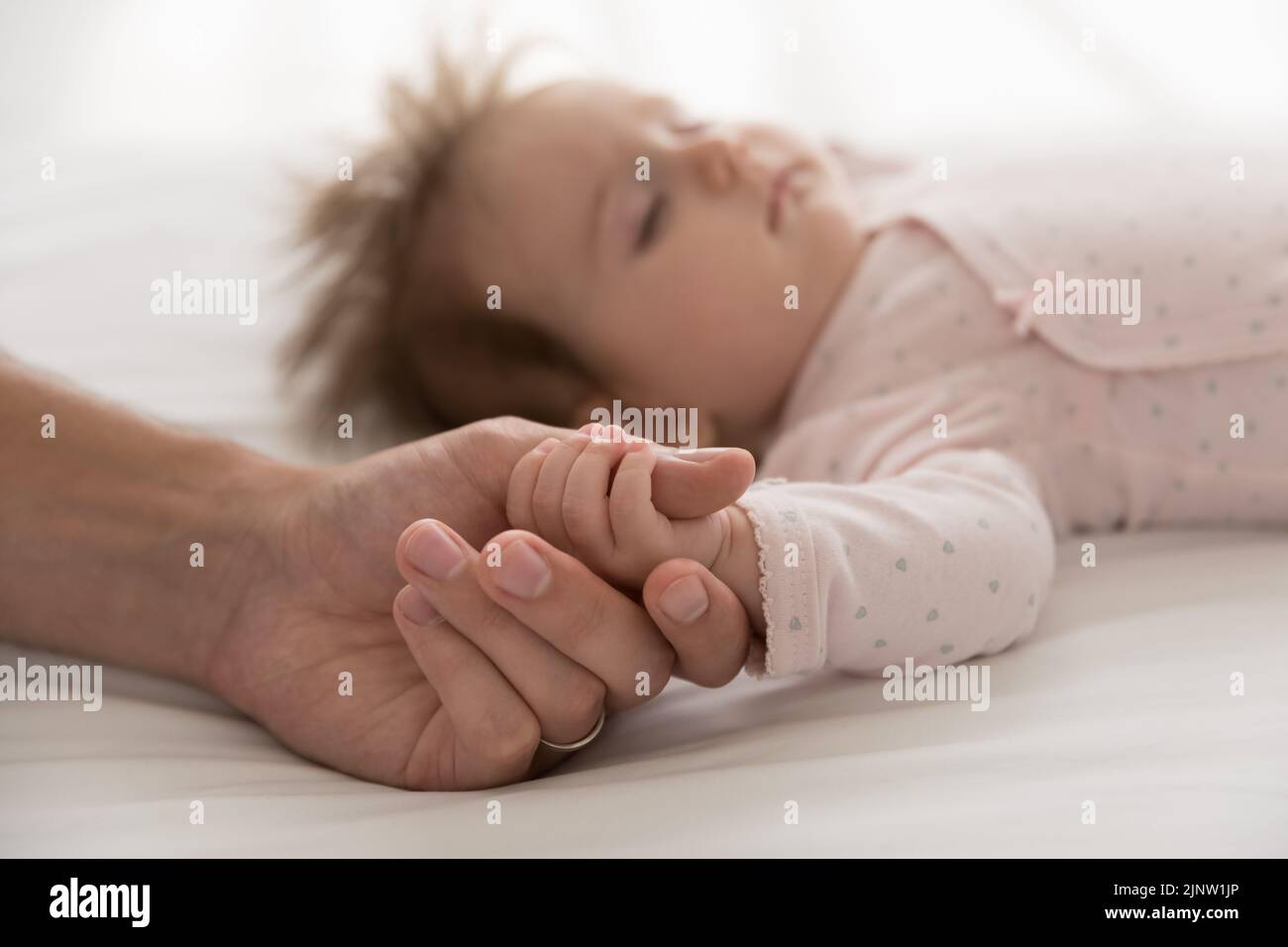 Papá amoroso sostiene el brazo minúsculo de la hija recién nacida que duerme linda Foto de stock