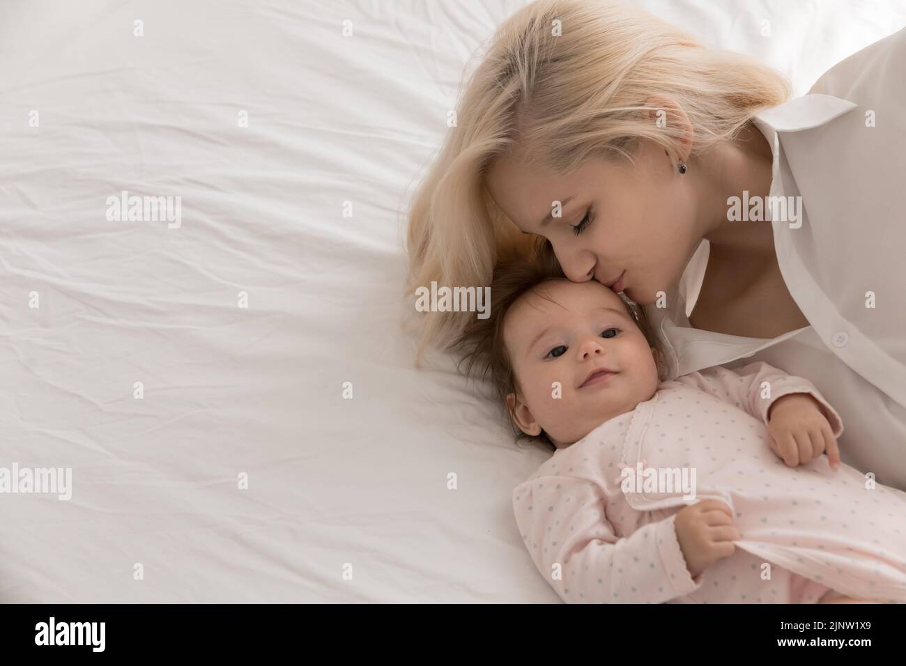 Joven madre amorosa besos en la frente de su hermoso recién nacido Foto de stock
