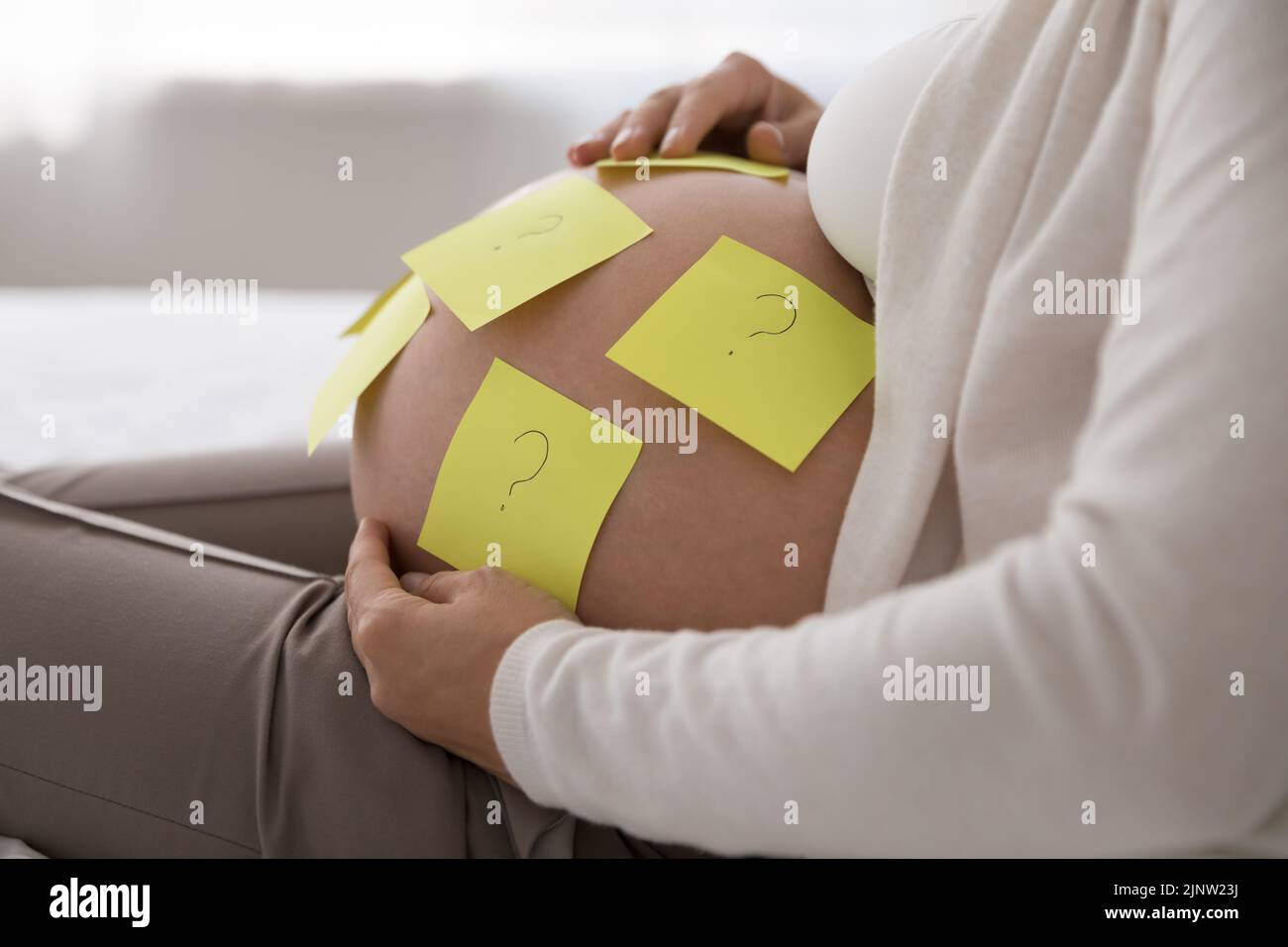 Adjuntamos notas adhesivas con preguntas sobre el vientre de la mujer embarazada Foto de stock