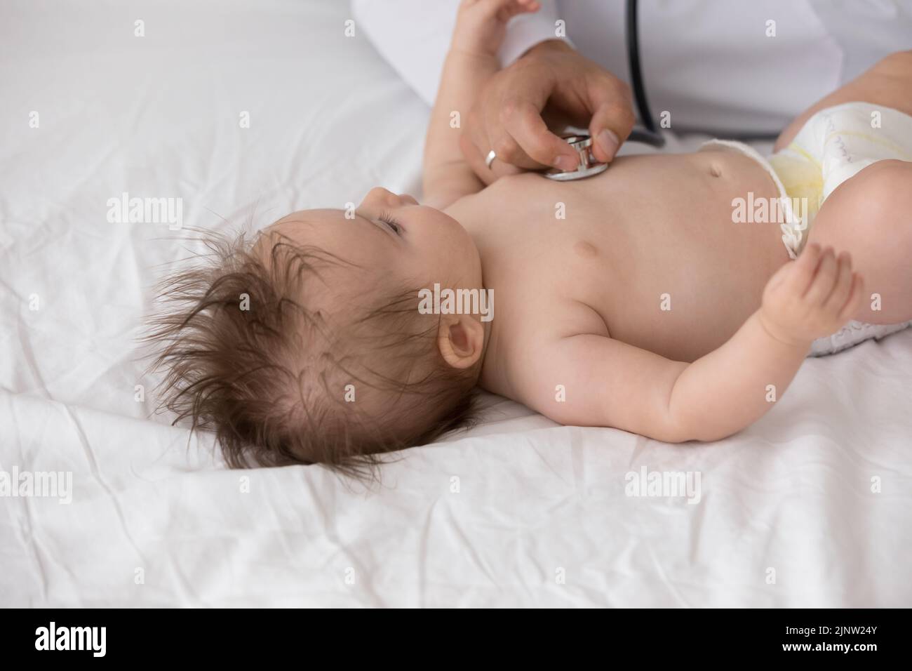 Un doctor desconocido sostiene que el estetoscopio escucha el latido del corazón del recién nacido, cerca Foto de stock