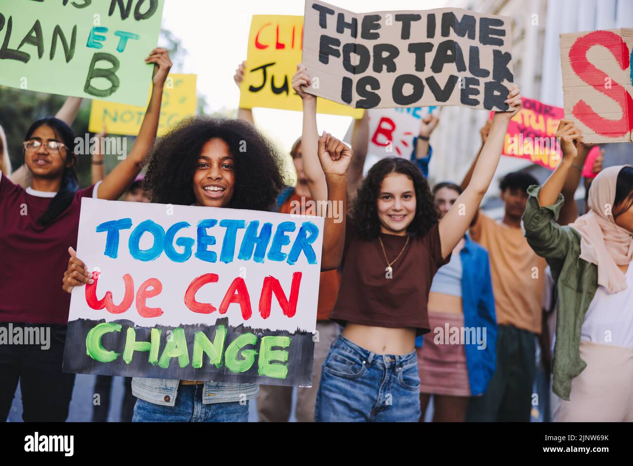 Protesta juvenil contra el cambio climático. Grupo de jóvenes activistas multiculturales que llevan carteles y pancartas mientras marchan contra el calentamiento global. Feliz Foto de stock
