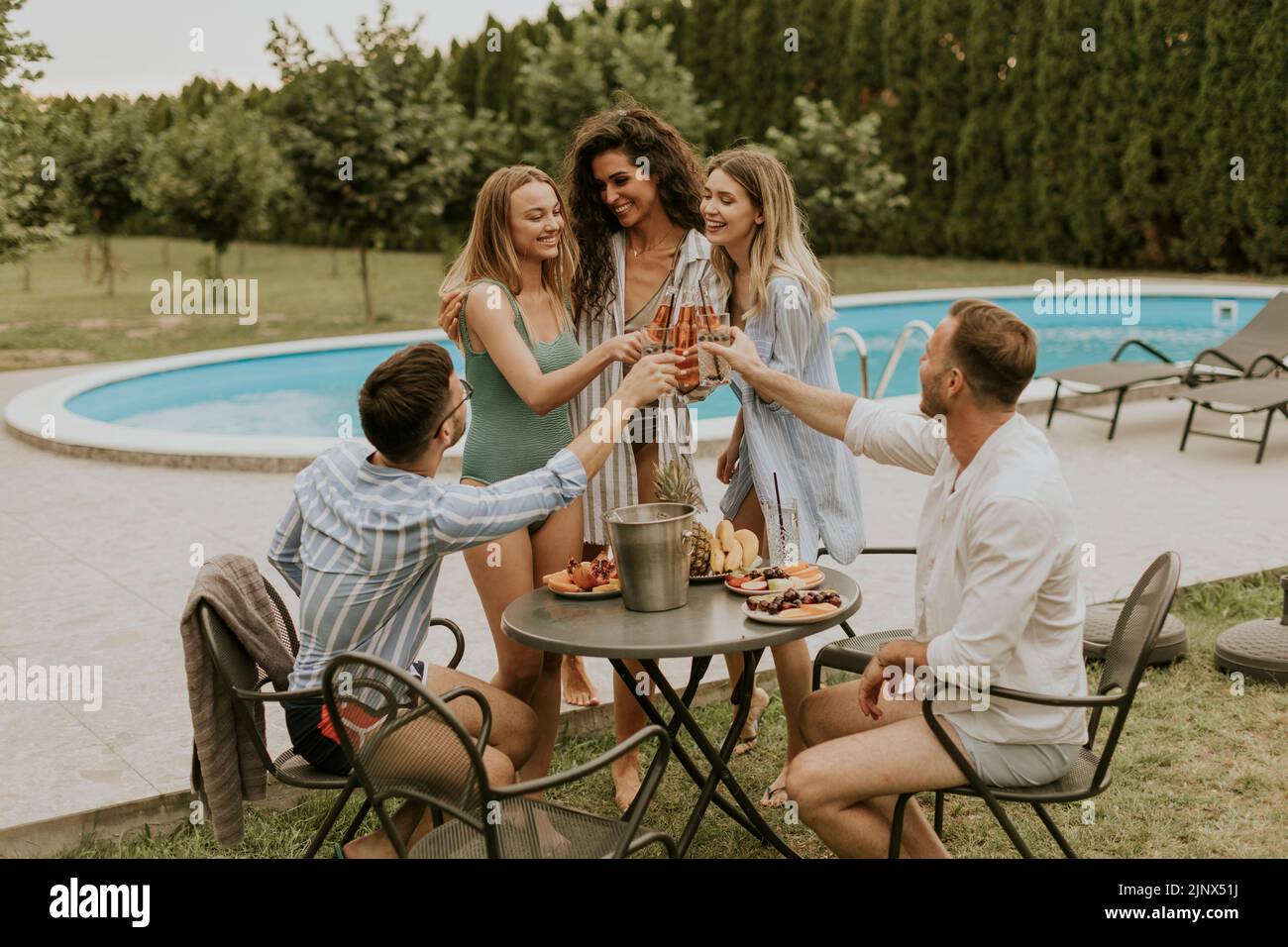 Grupo de jóvenes felices animando con sidra junto a la piscina en el jardín Foto de stock
