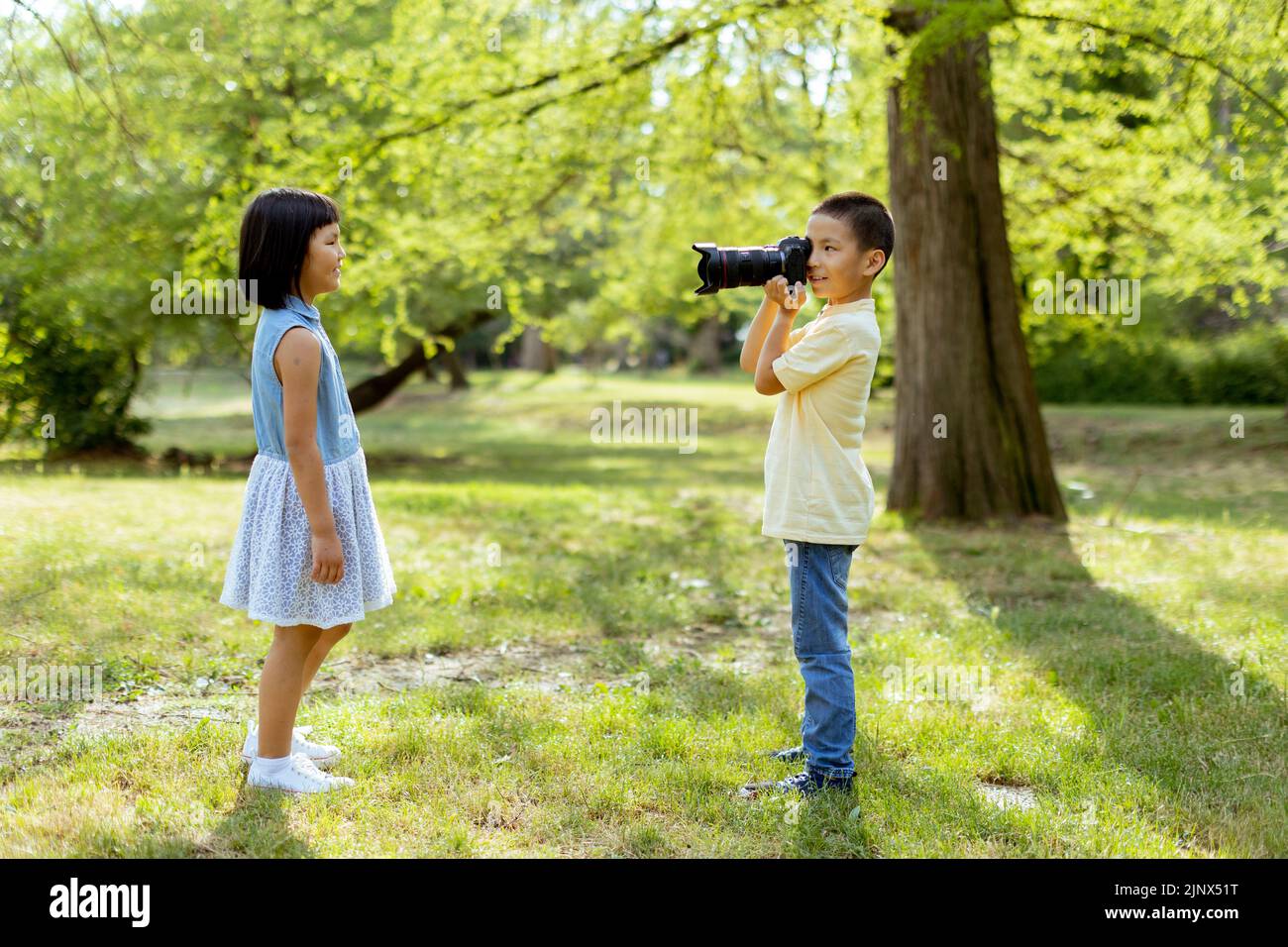 Lindo niño asiático actuando como un fotógrafo profesional mientras toma fotos de su hermana pequeña Foto de stock