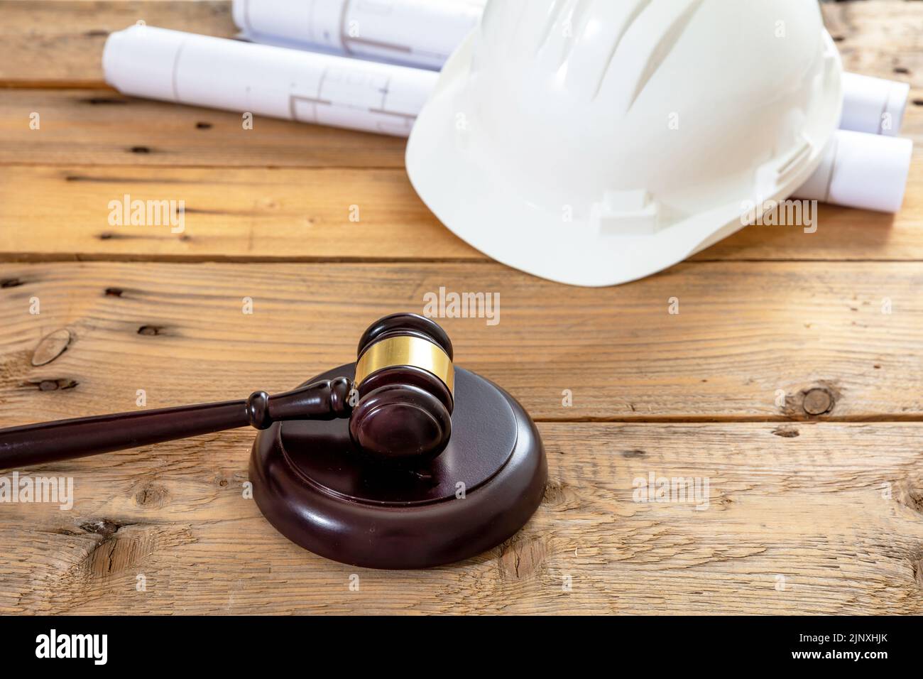 Construcción, Derecho laboral. El casco de seguridad del ingeniero de color blanco, el martillo del juez y los planos de construcción sobre una mesa de madera Foto de stock