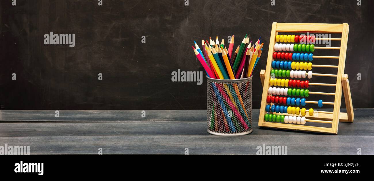 Plantilla de regreso al colegio. Lápices de colores y Abacus en el salón de clase escritorio de madera azul, fondo de pizarra, espacio de copia Foto de stock